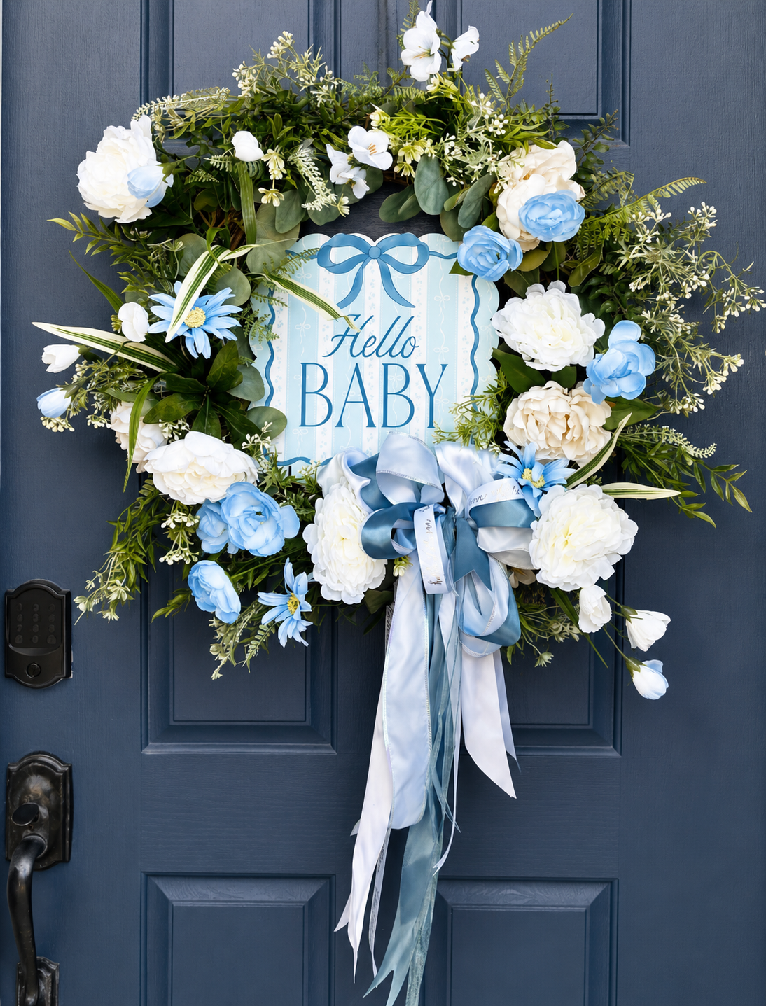 Blue and white floral wreath with a sign that says "Hello Baby" hanging on a dark blue door.