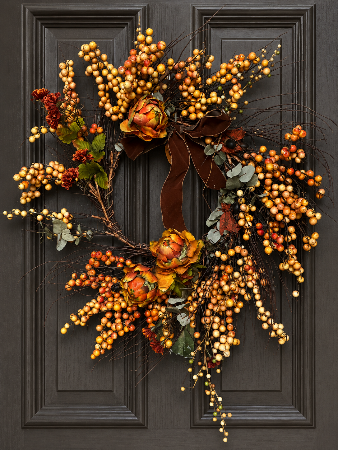 Autumn-themed decorative wreath with berries, flowers, eucalyptus, and a brown ribbon on a black door