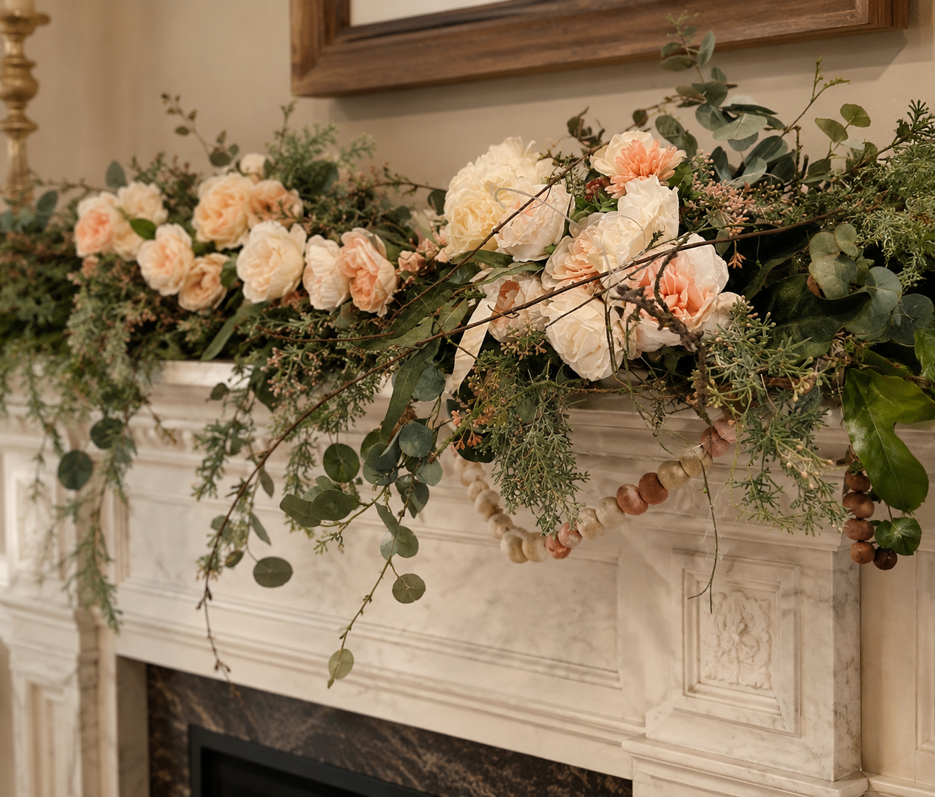 A floral arrangement with cream and peach-colored roses, green foliage, and eucalyptus branches on a decorative white fireplace mantel.
