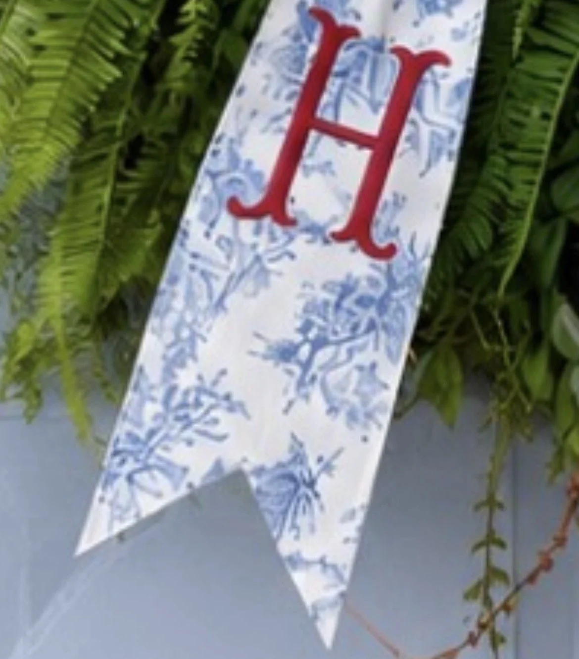 Decorative banner with red letter 'H' hanging among green foliage.