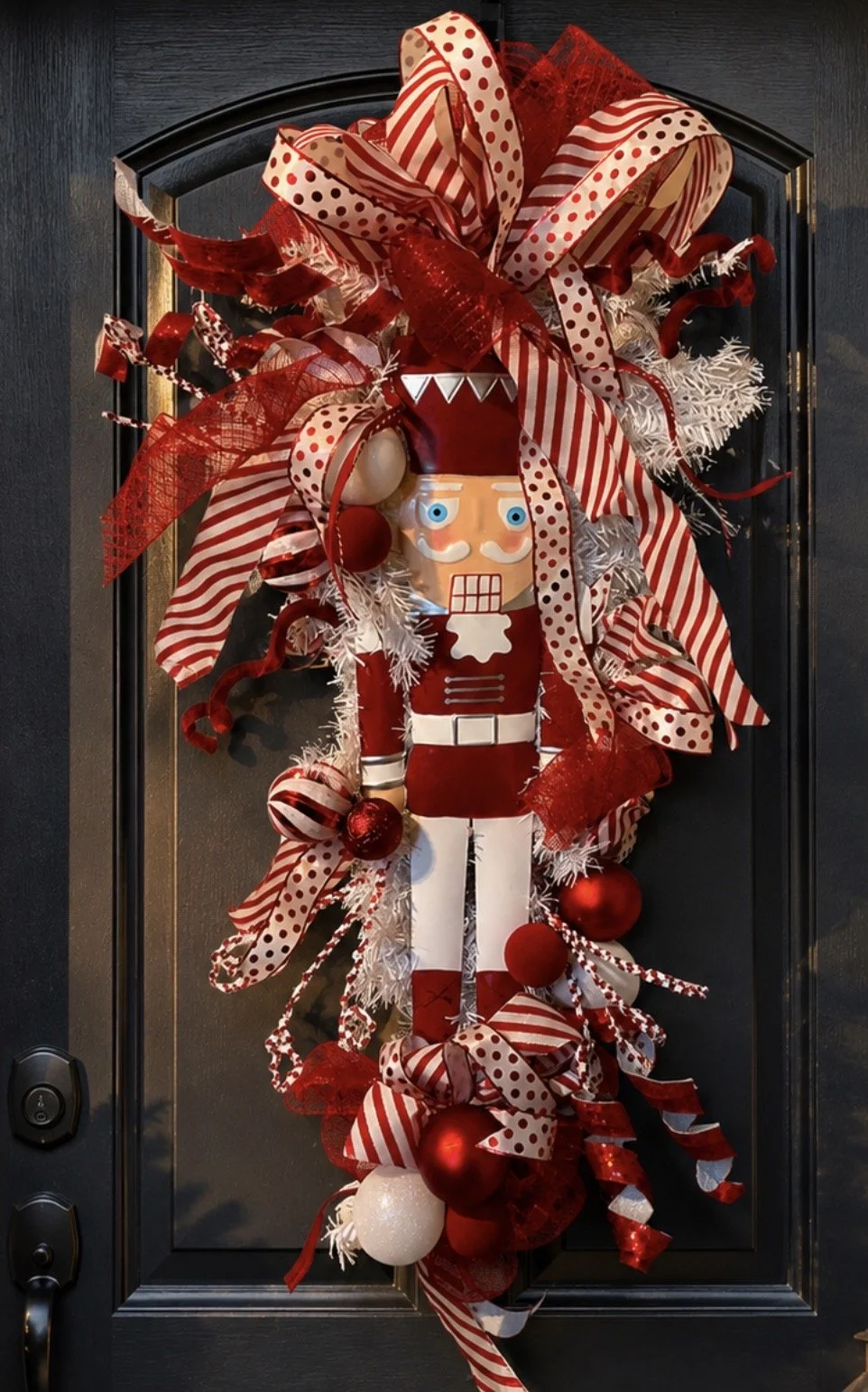 Christmas wreath on a black door decorated with red and white ribbons, ornaments, and a nutcracker figure