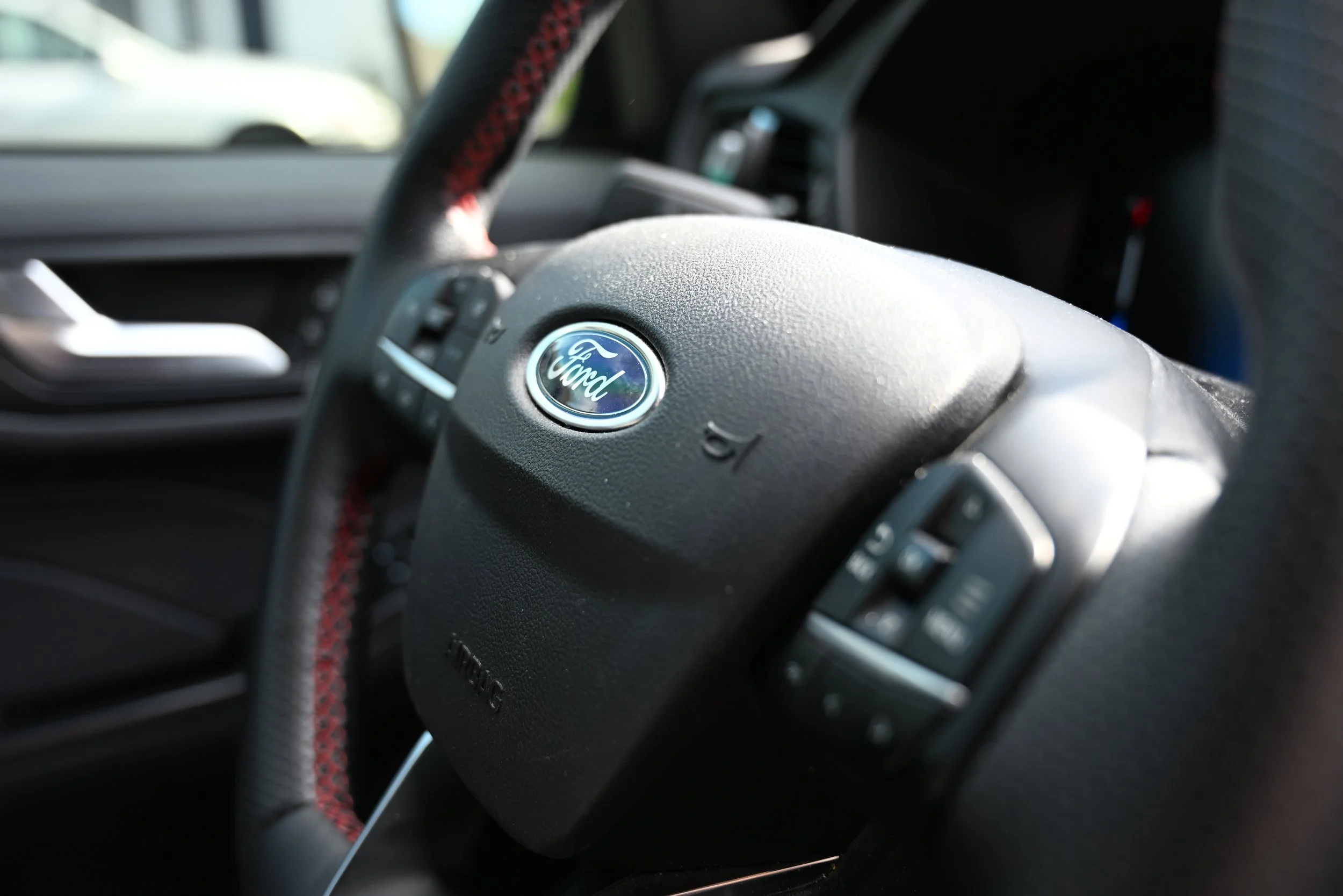 Close-up of a Ford steering wheel inside a vehicle, with dashboard elements visible in the background.