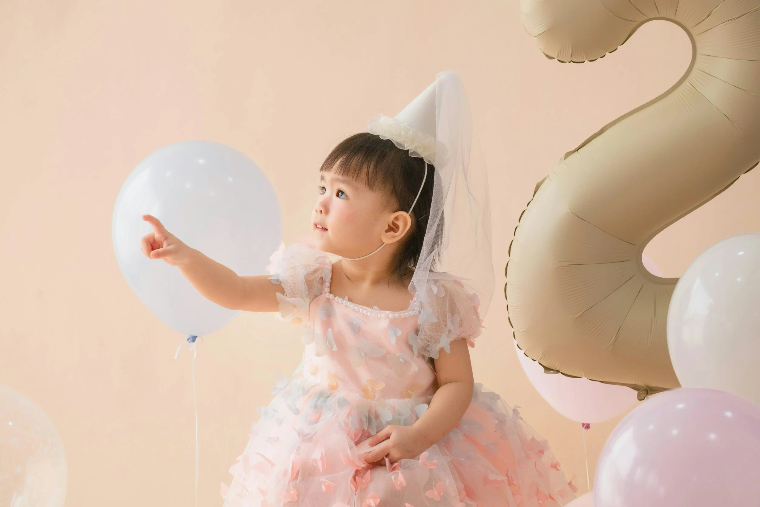 Toddler in a party dress reaching for a white balloon