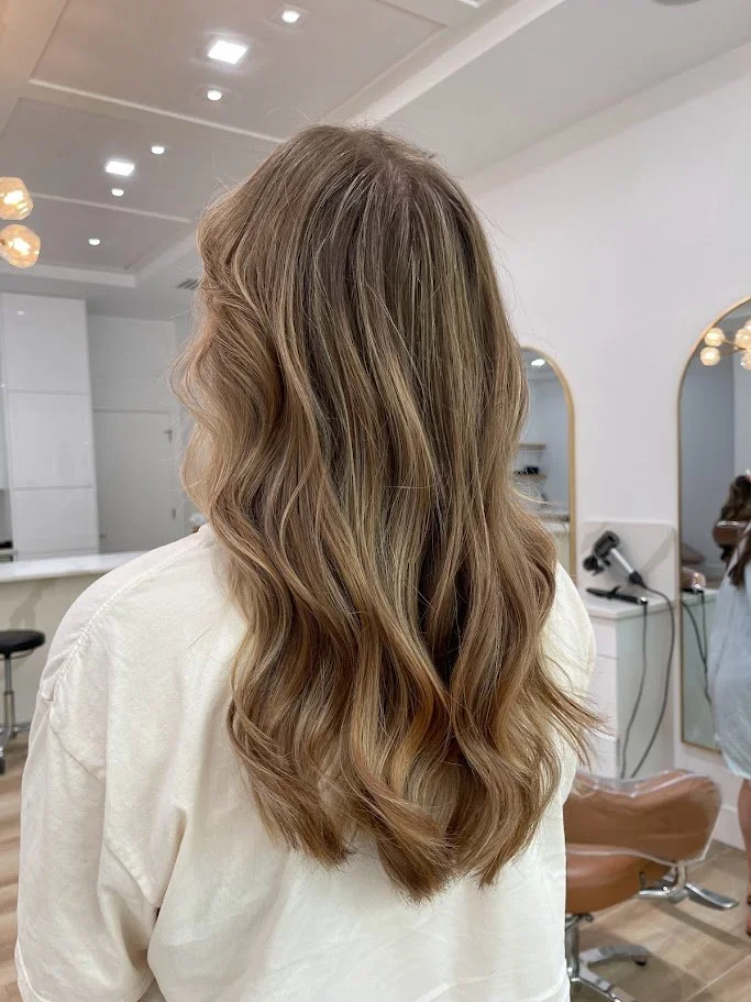 Back of a woman with long, wavy, light brown hair in a salon.