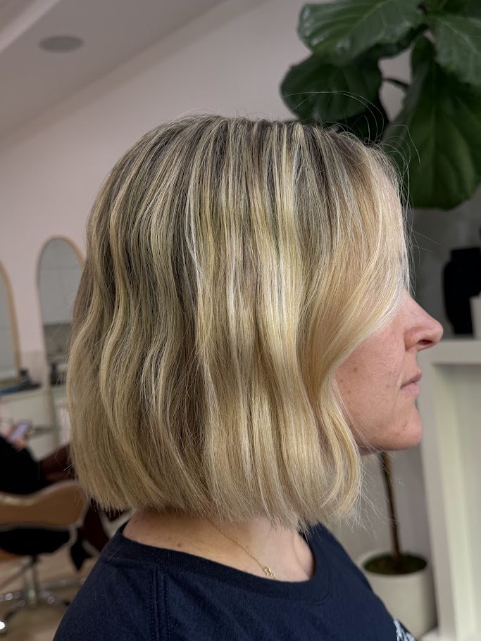 Side profile of a woman with shoulder-length blonde wavy hair in a salon setting.