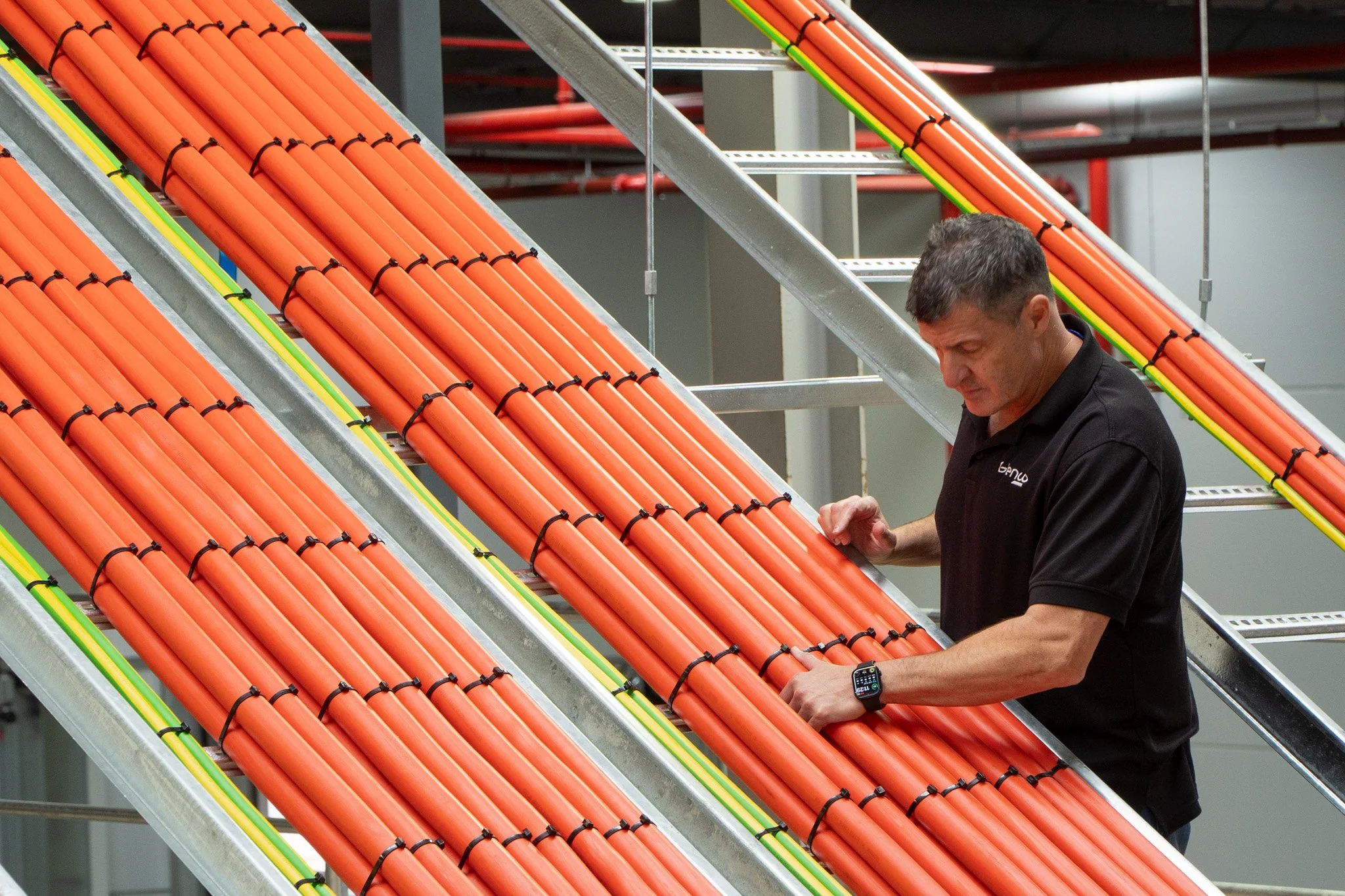 A man working on orange cables on a ladder in an industrial or utility environment.