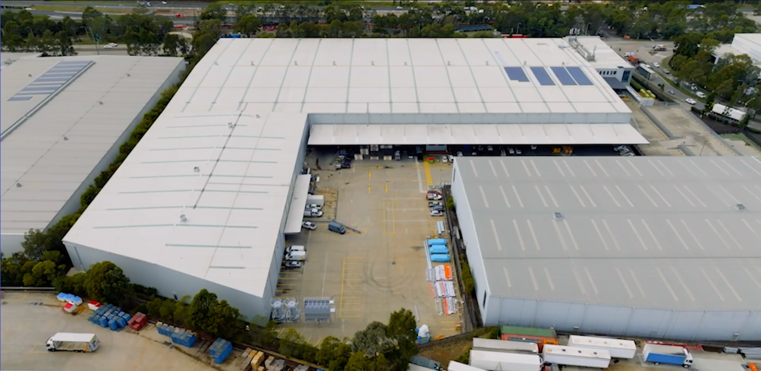 Aerial view of large industrial warehouse buildings with parking lot and trucks nearby.