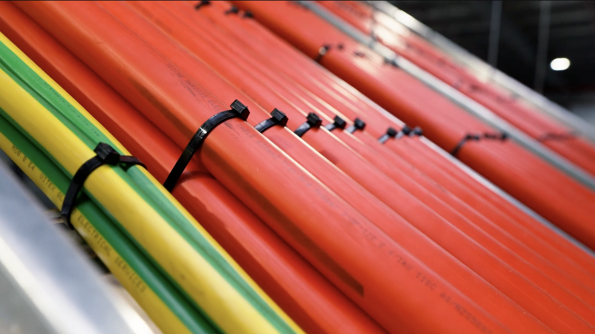 Close-up of red and yellow cables secured with black zip ties, organised in parallel lines, with a dark industrial background.