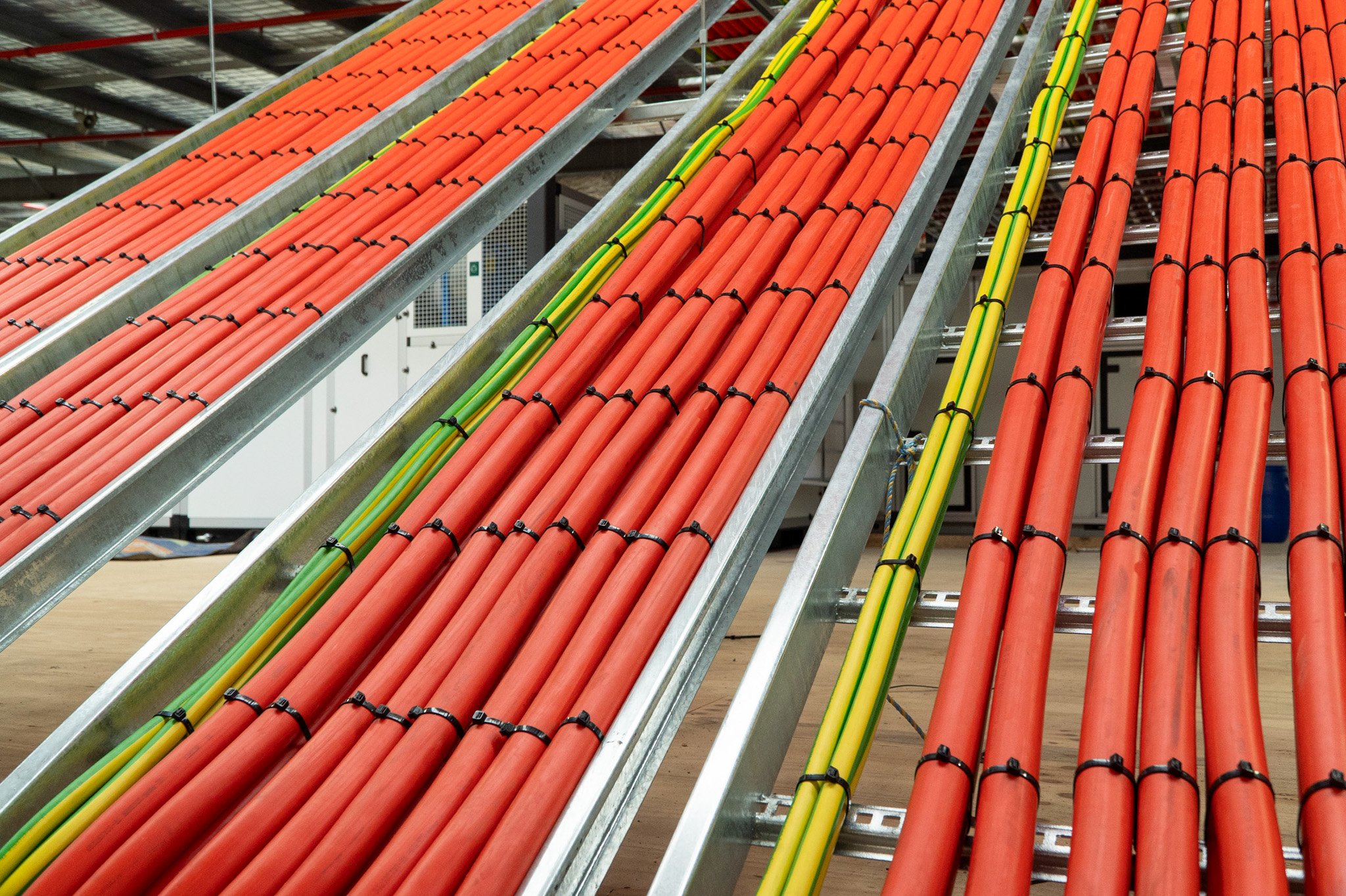 Multiple orange and yellow insulated electrical cables arranged on metal racking in an industrial setting.