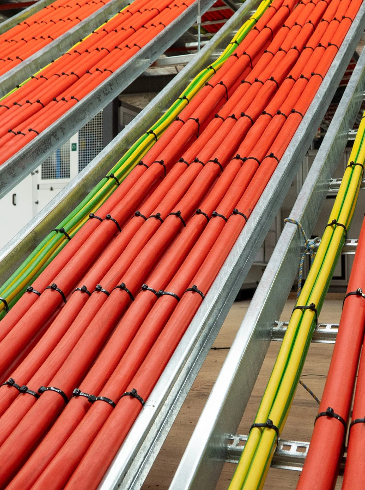 Multiple orange and yellow electrical conduits arranged on metallic racks, secured with black ties in an industrial setting.