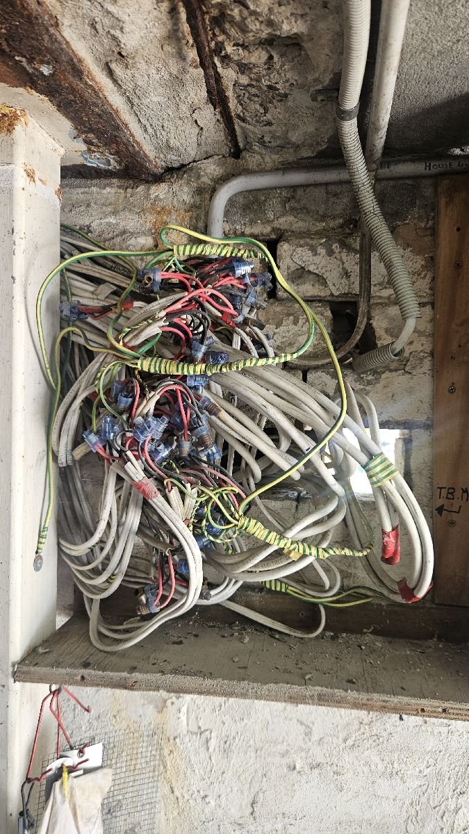 Electrical wiring mess in an unfinished wall, with tangled wires, circuit connectors, and exposed wiring.
