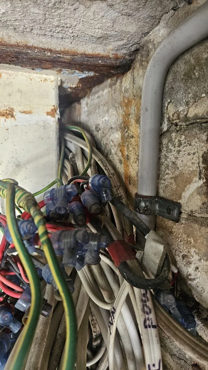 Close-up of electrical wiring and conduit near a brick wall, with some rust and corrosion visible.