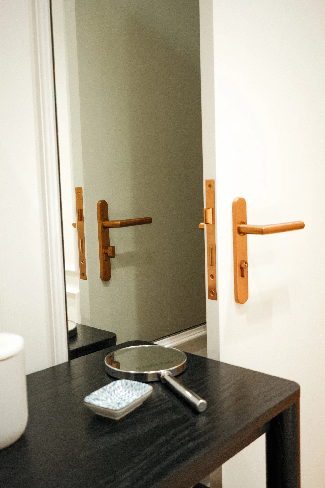 A bathroom with a sink, a mirror, and an open door revealing a closet area with wood door handles.