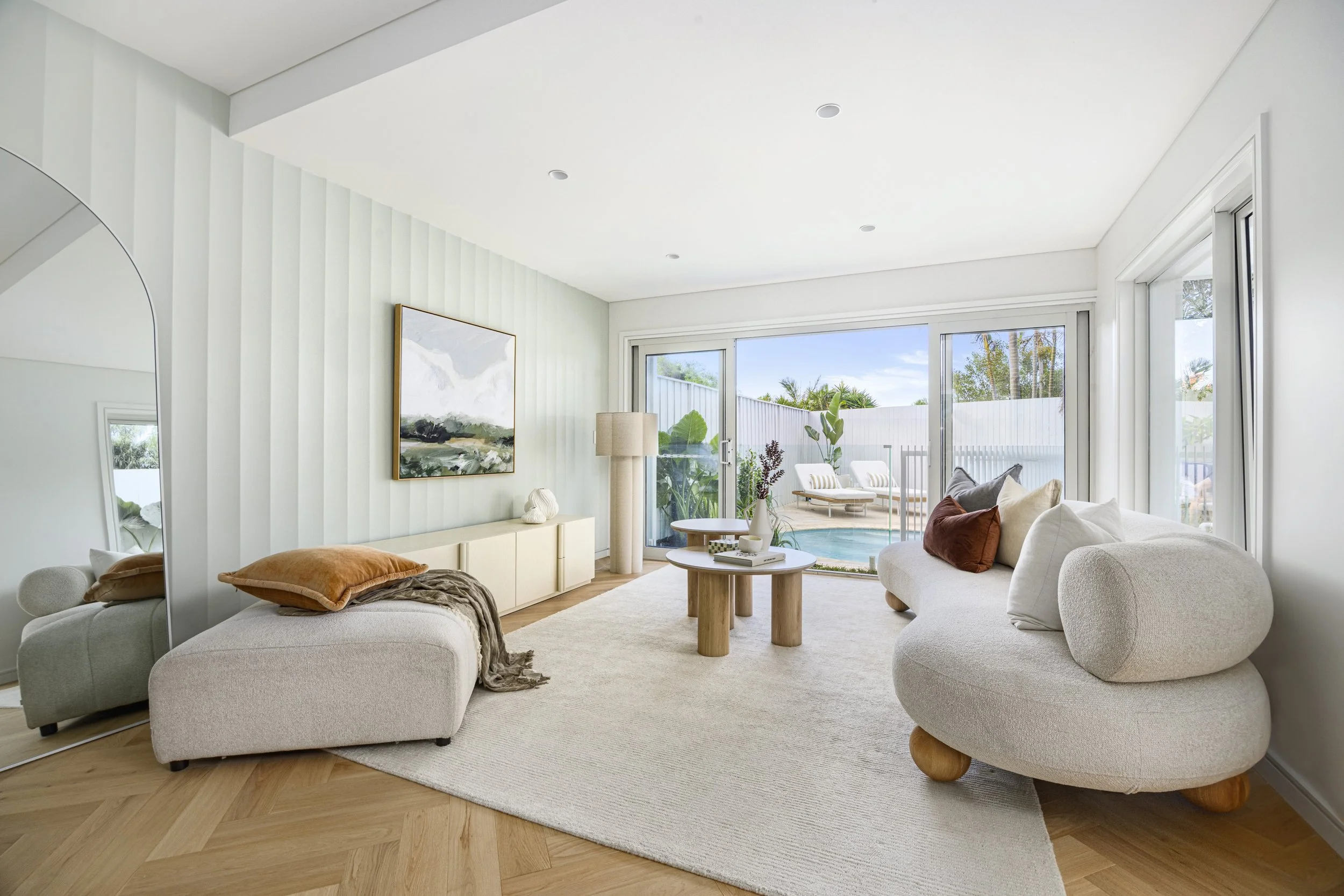 Living room with white sofa, ottoman, and beige pillows, large window with sliding glass door leading to patio, abstract wall art, and modern decor.