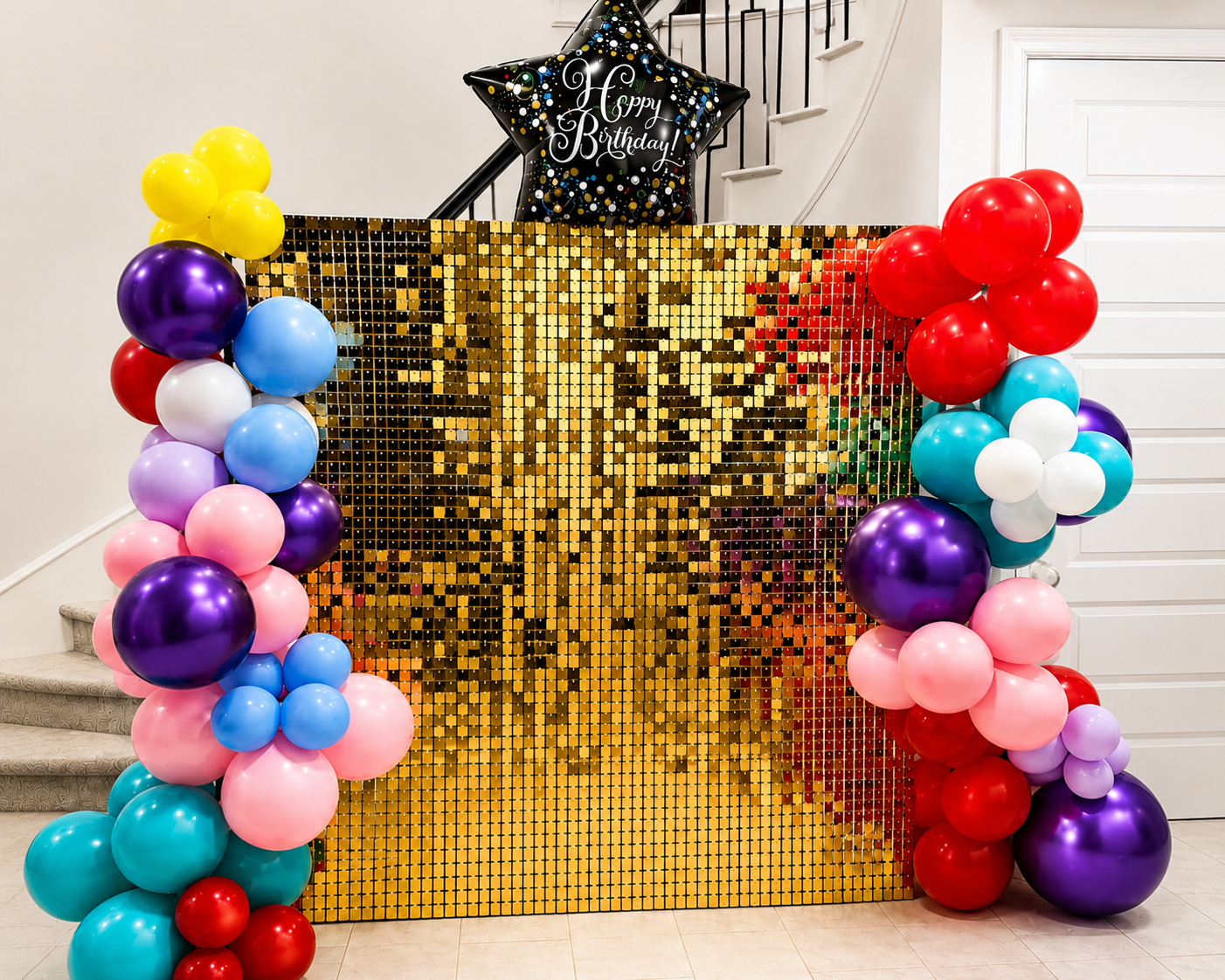 Colorful birthday party decoration with balloons and a gold mirrored backdrop. The balloons are arranged in clusters on both sides of the backdrop, featuring red, blue, purple, pink, white, yellow, and teal colors. A black star-shaped balloon with 'Happy Birthday!' written on it is at the top center.