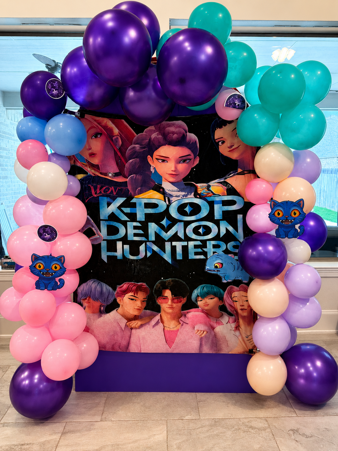 Decorative K-pop Demon Hunters poster surrounded by colorful balloons, including purple, pink, light blue, and white, with cartoon cat and dinosaur cutouts.