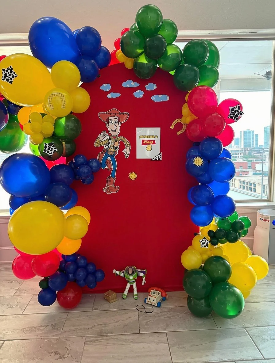 Colorful balloon display with a Toy Story theme, featuring Woody, Buzz Lightyear, and decorations resembling clouds and cow print accents.