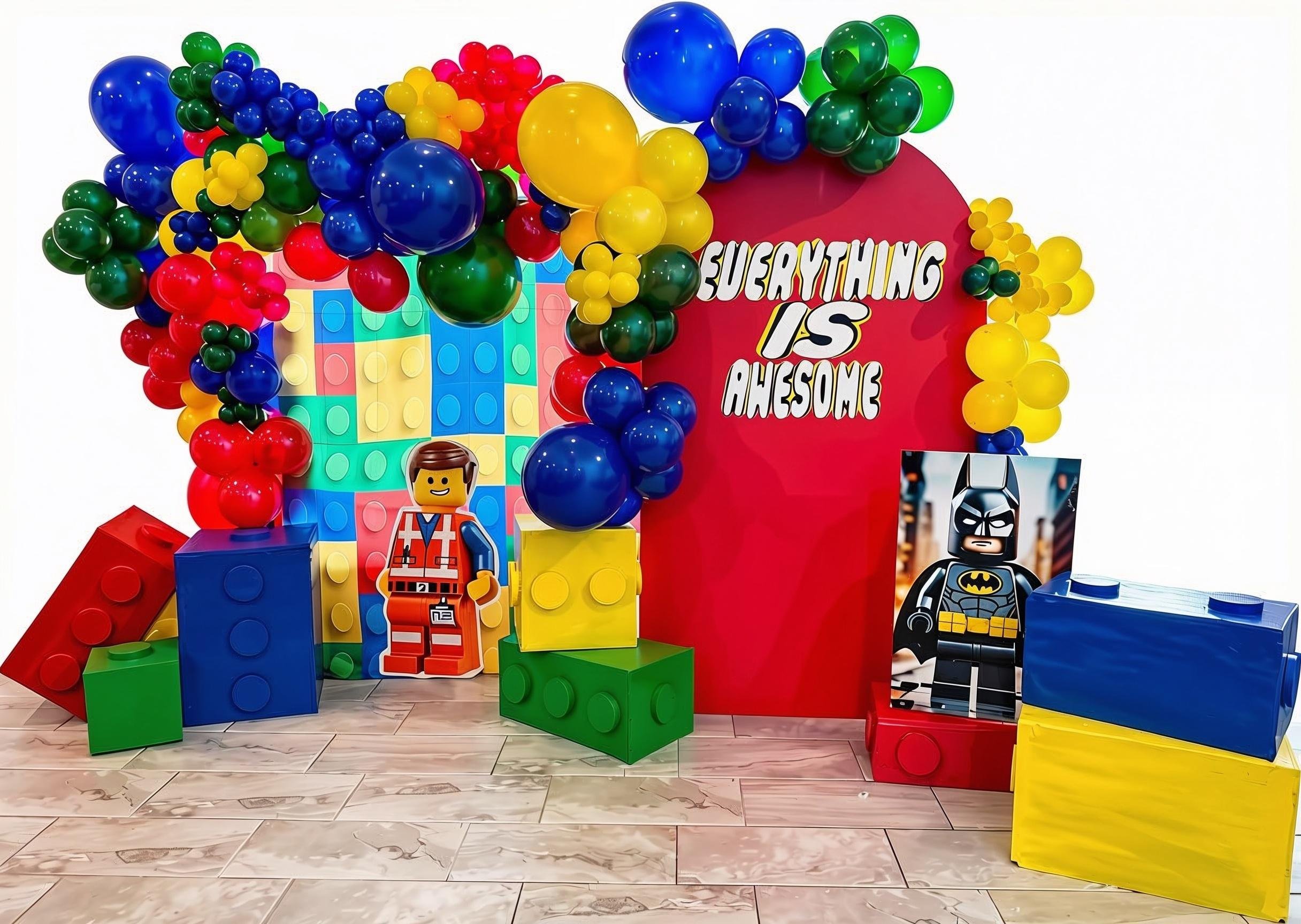 Colorful party decoration with large building blocks, balloons, and superhero figures, including Batman, with a red backdrop that says "Everything Is Awesome."