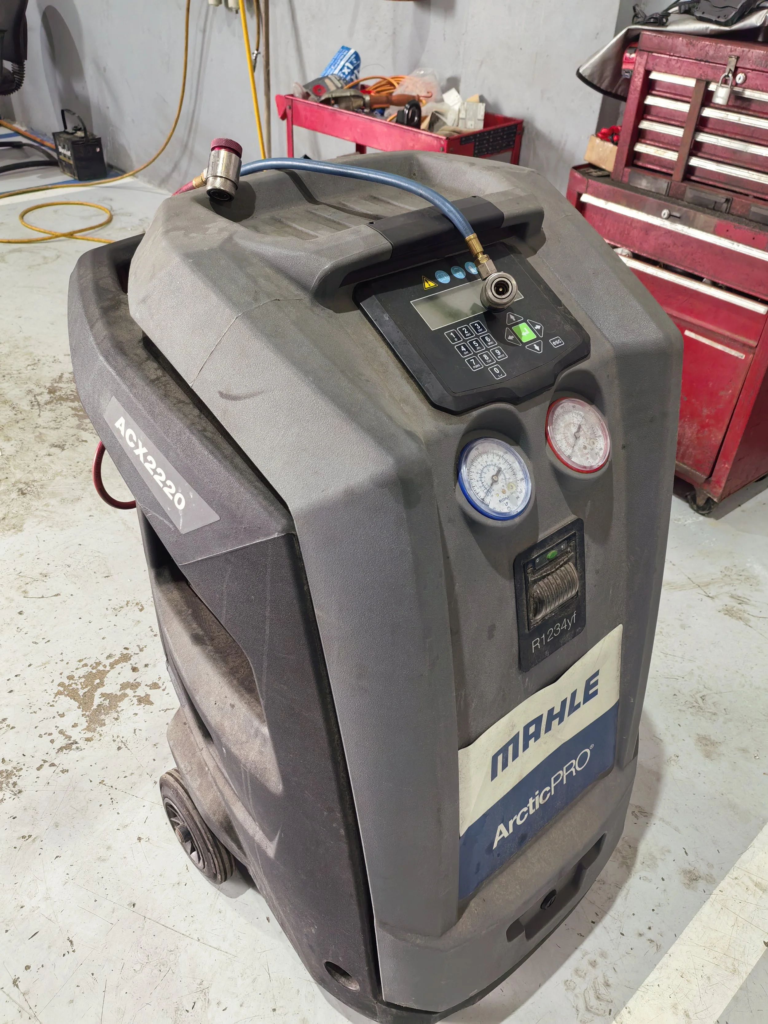 Aparato de refrigeración portátil marca ArcticPRO, con medidores y panel de control, en taller de reparación con herramientas y estanterías en el fondo.