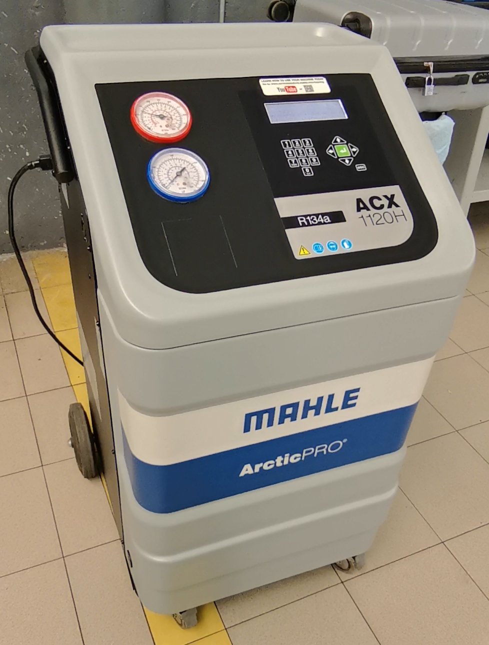 Aparato de refrigeración de refrigerante R134a de la marca MAHLE, modelo ArcticPRO, con manómetros y control digital en una superficie de cerámica.