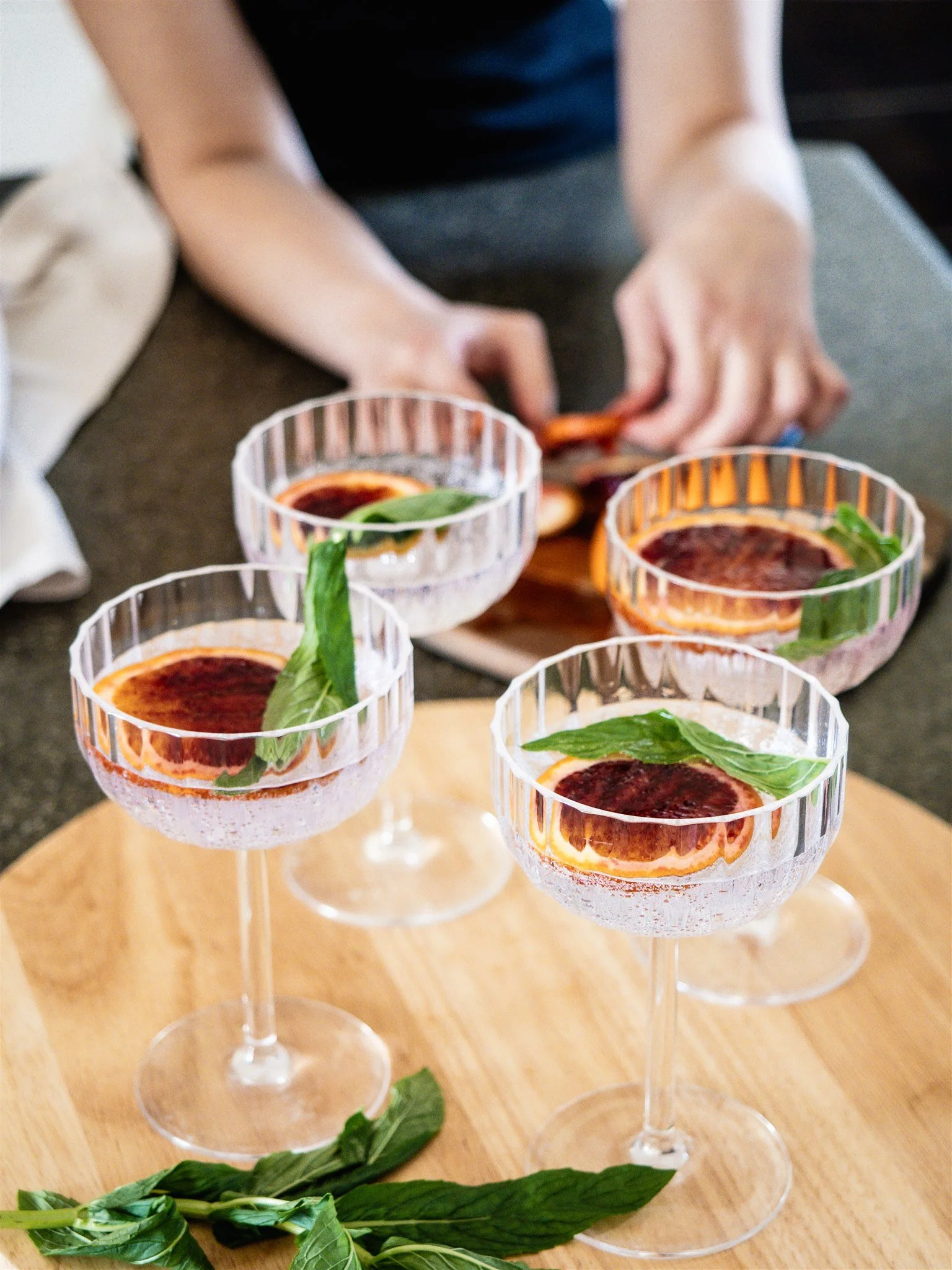 Six glasses of Negroni cocktails garnished with basil leaves, arranged on a wooden surface.