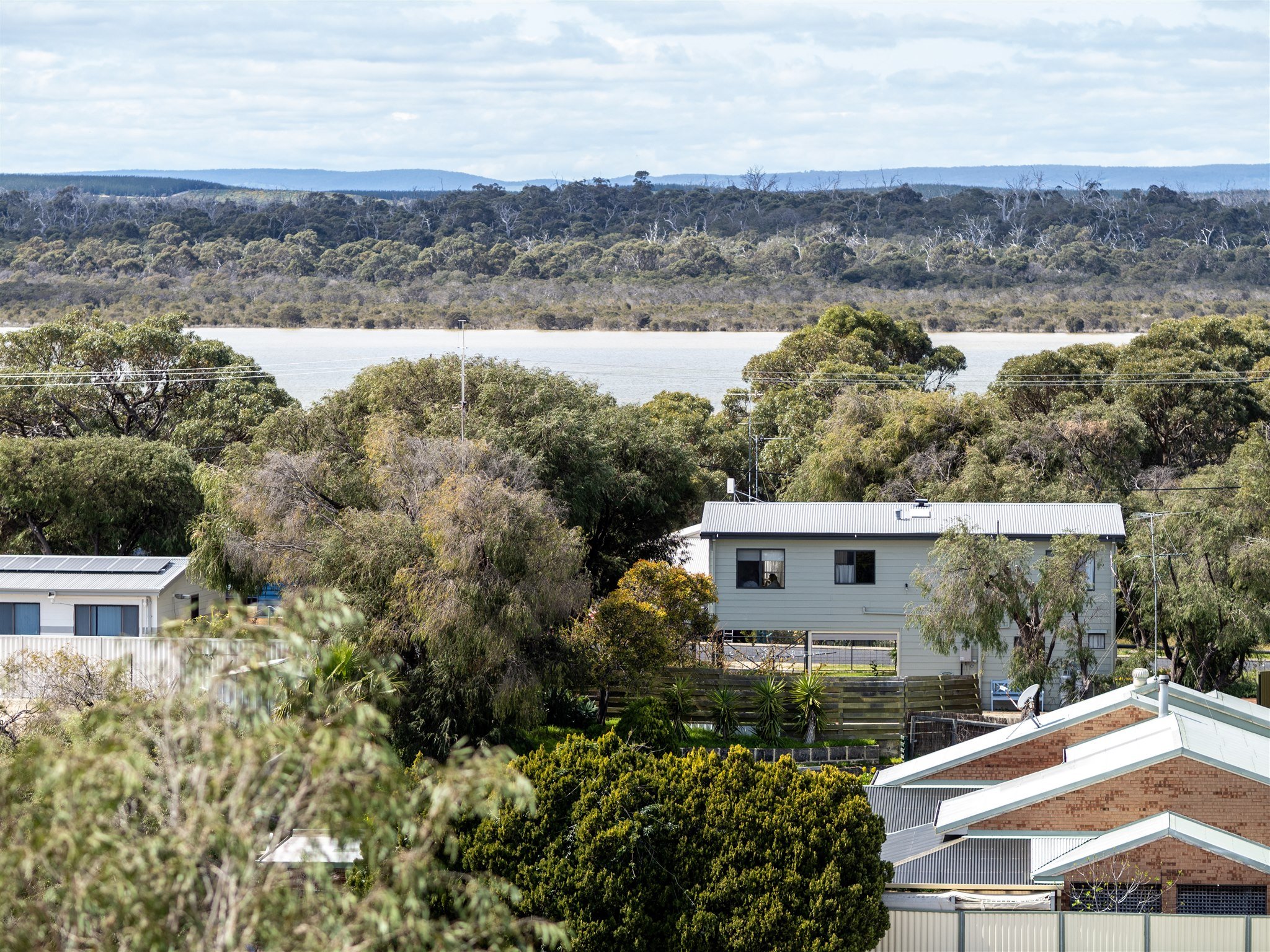 A suburban neighborhood with houses, trees, and a distant body of water under a cloudy sky.