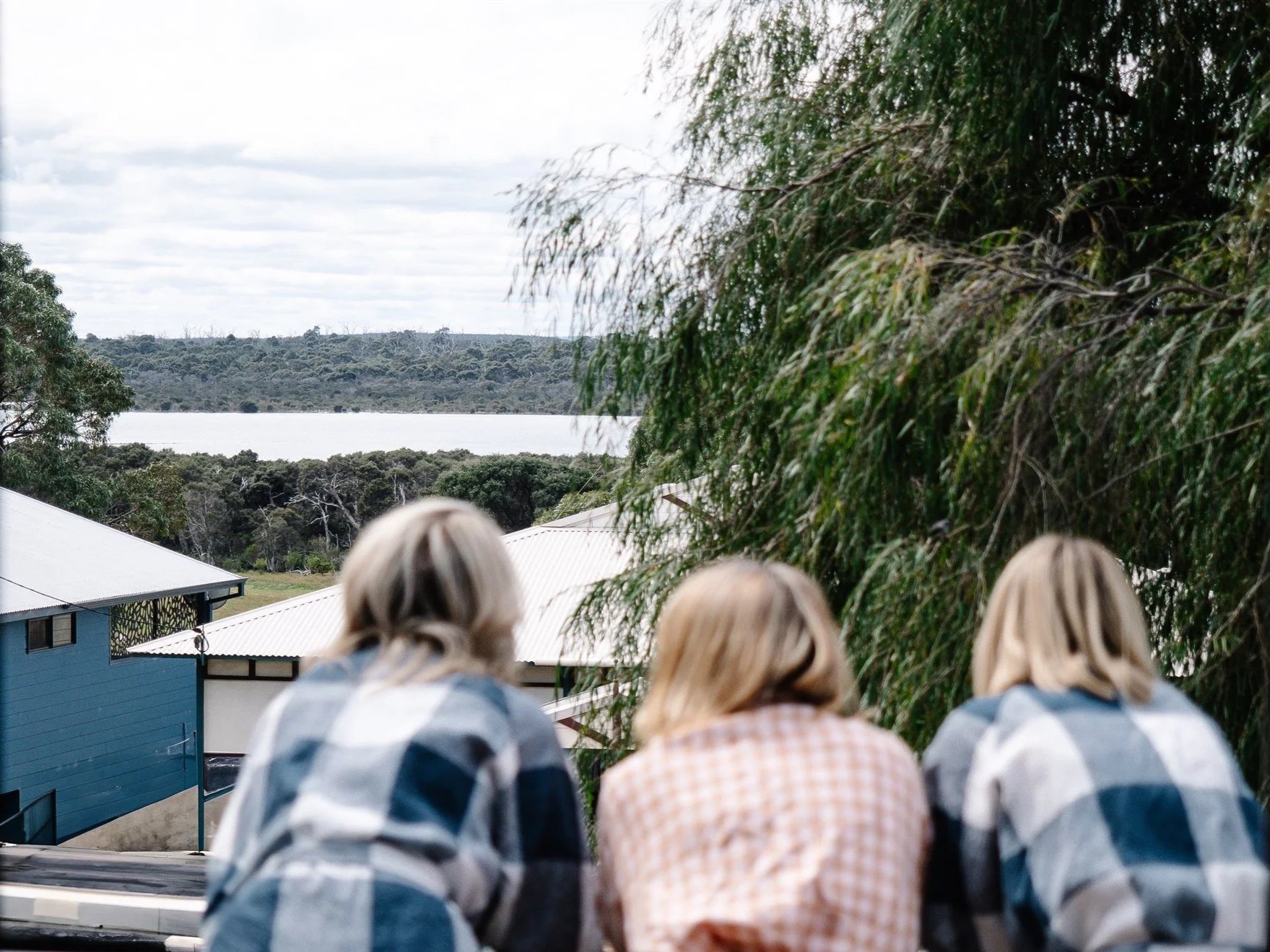 View of a lake with trees and hills in the background, seen from a rooftop with several heads of people in the foreground.