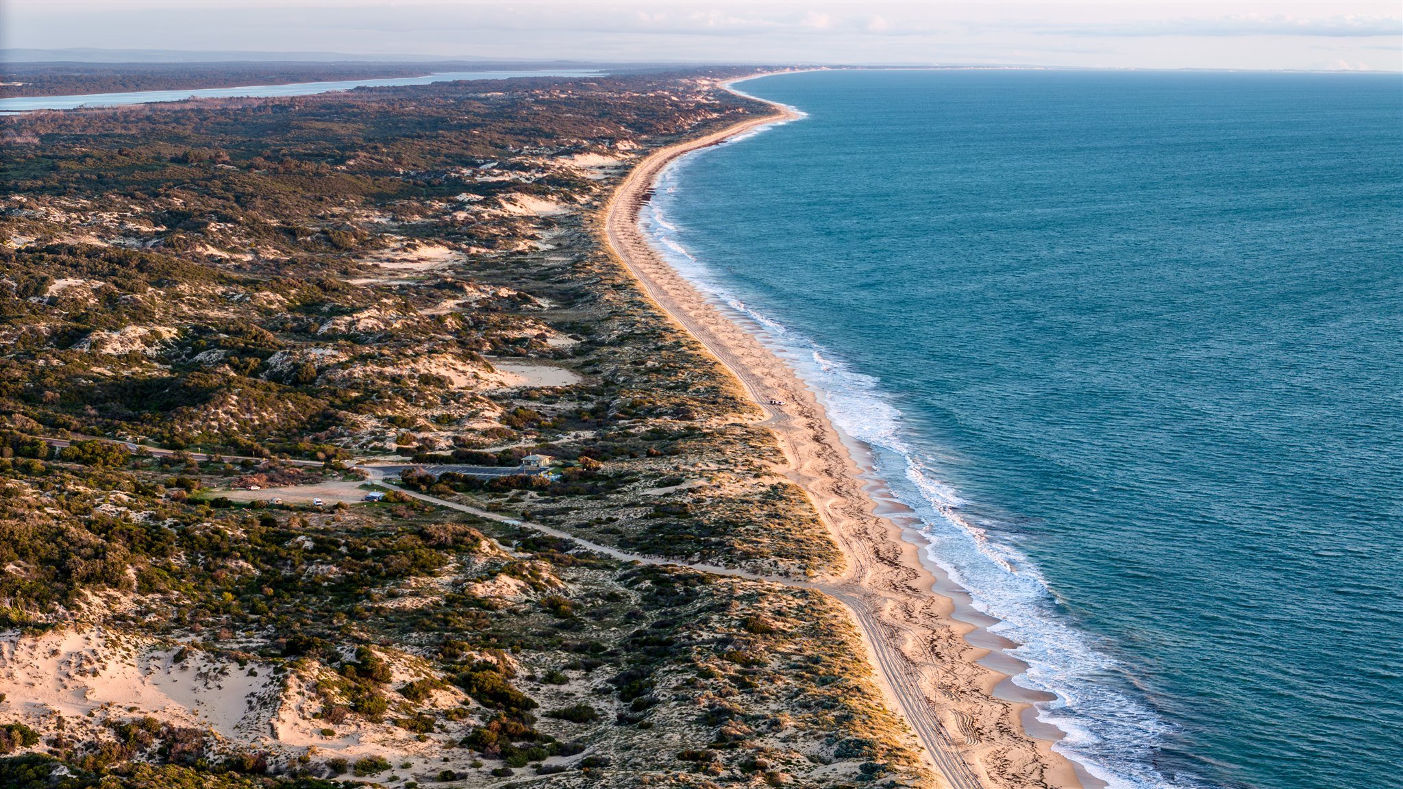 Aerial view of a coastal landscape showing sandy beaches, rocky dunes, green vegetation, and the Atlantic Ocean.