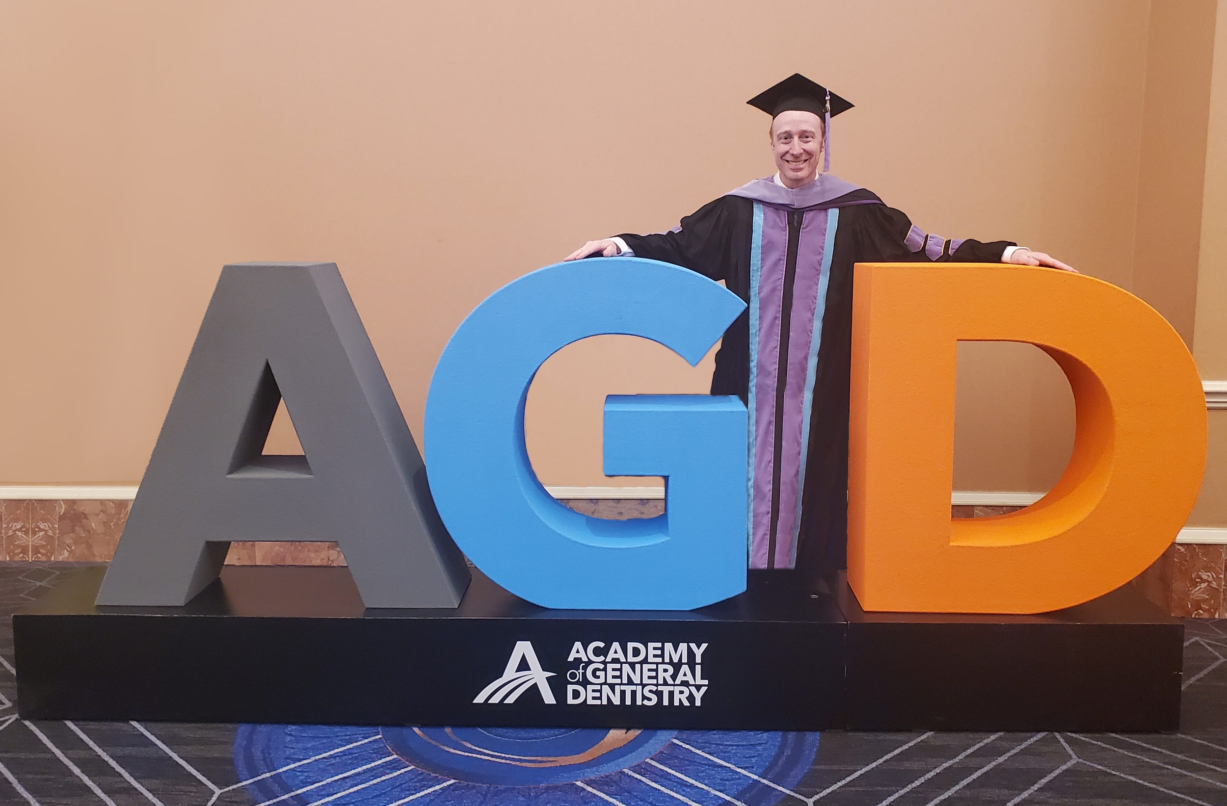 Dr. Ryan Cormack in graduation regalia behind an Academy of General Dentistry display