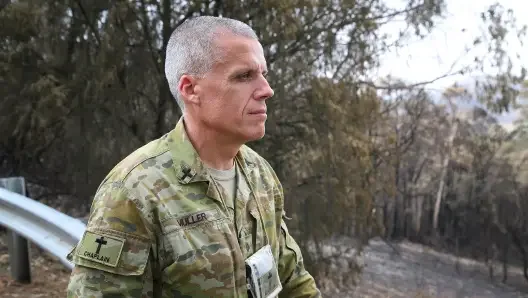 A soldier in camouflage uniform standing outdoors next to a guardrail.