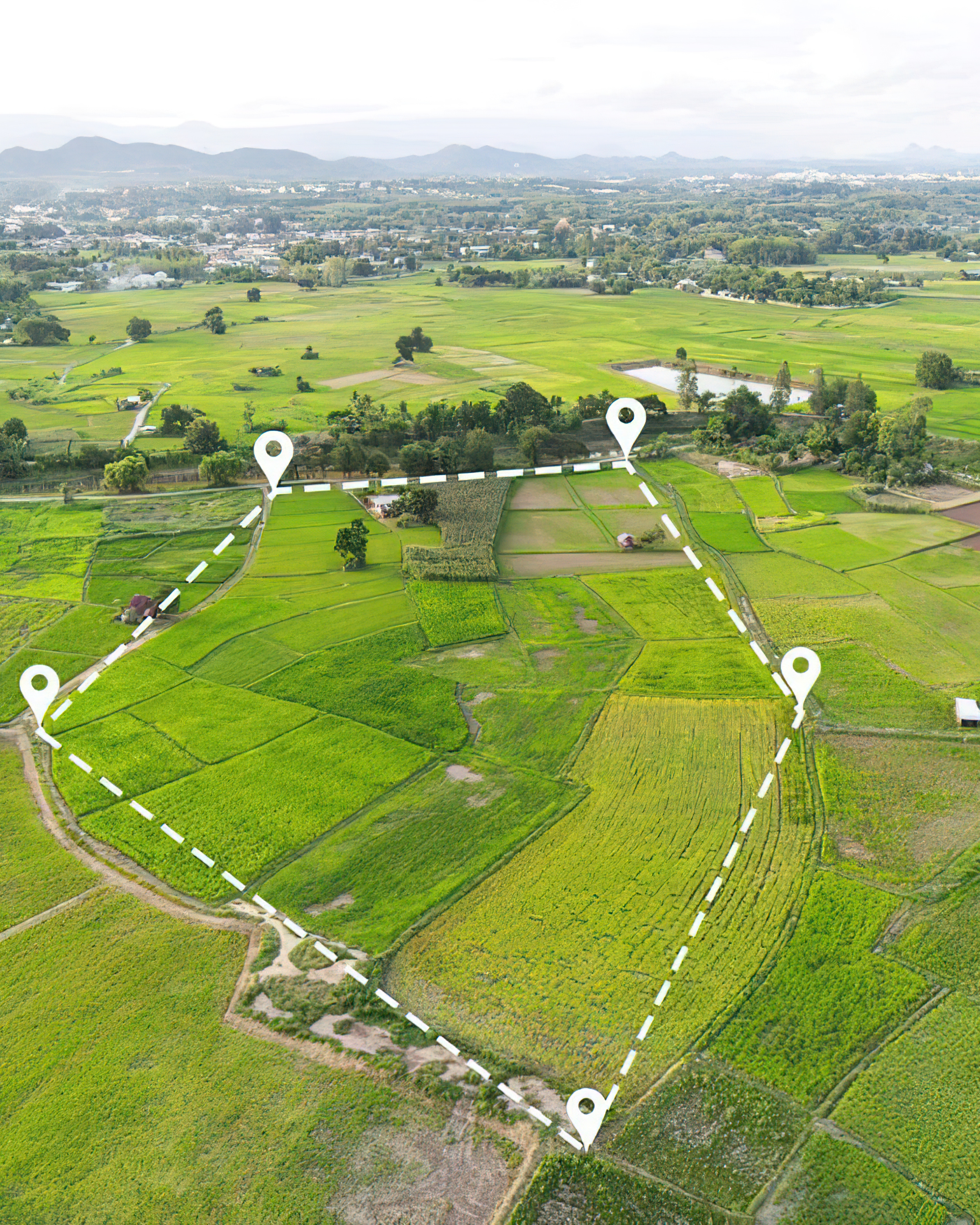 Aerial view of green farmland with marked route, small buildings, and distant mountains.