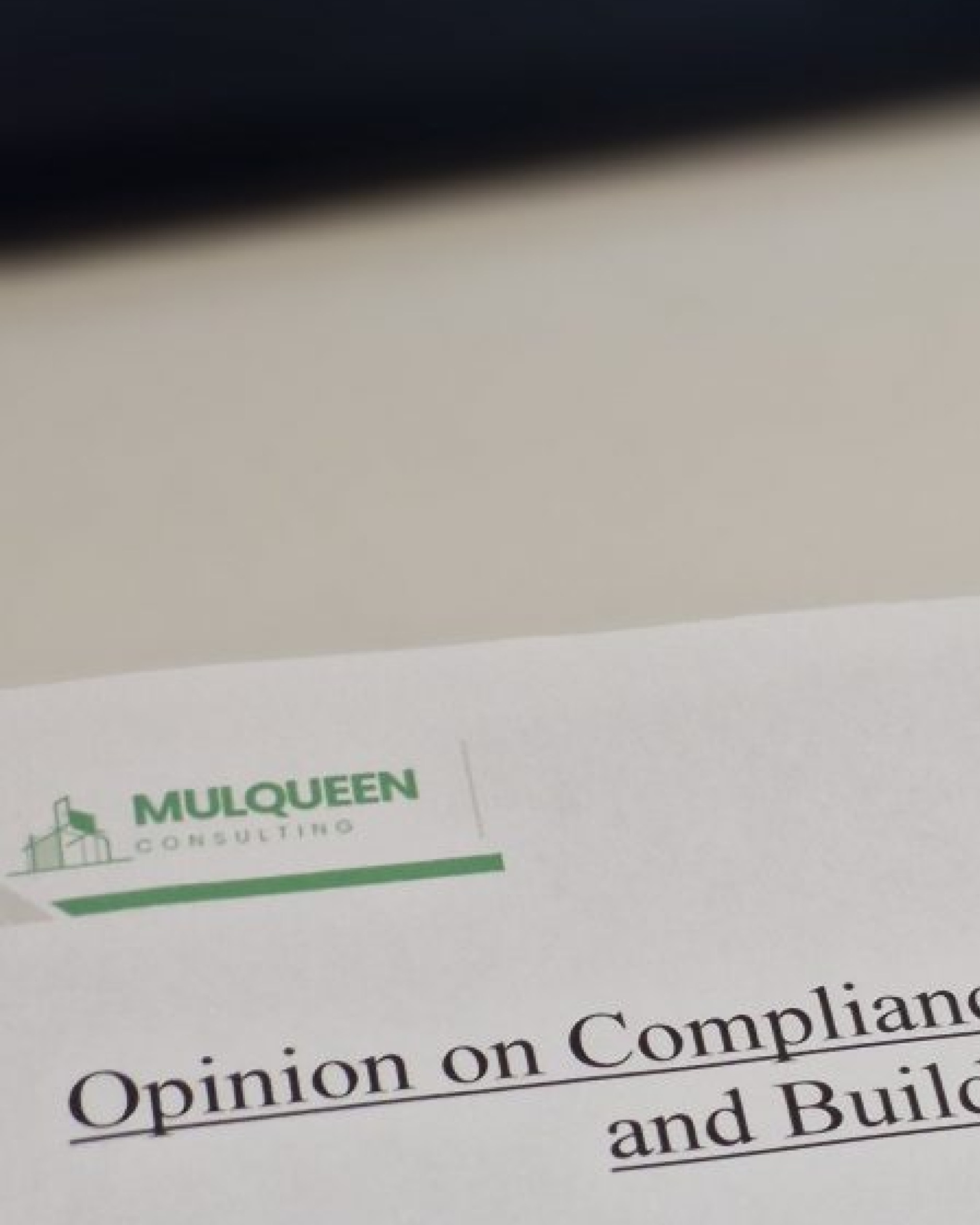 Close-up of a document page with text about opinion on compliance, partially visible, from Mulqueen construction, with a logo and green accents.