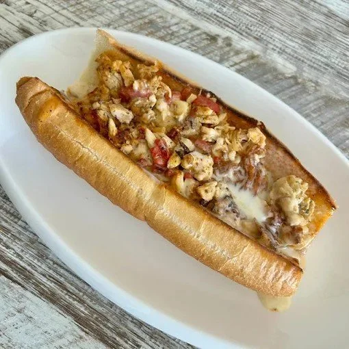 A Philly cheesesteak sandwich with beef, melted cheese, and chopped onions and tomatoes in a hoagie bun, served on a white oval plate.