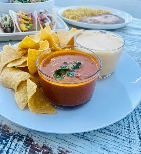 Plate with nachos, salsa, and sour cream, with refried beans and rice in the background.