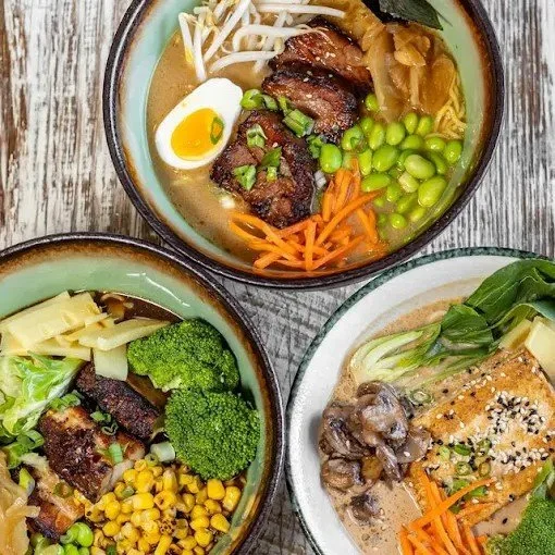 Three bowls of Asian cuisine, including ramen with beef, boiled egg, bean sprouts, green onions, and carrots; a bowl of broccoli, corn, and beef; a bowl of tofu, mushrooms, and vegetables in broth.