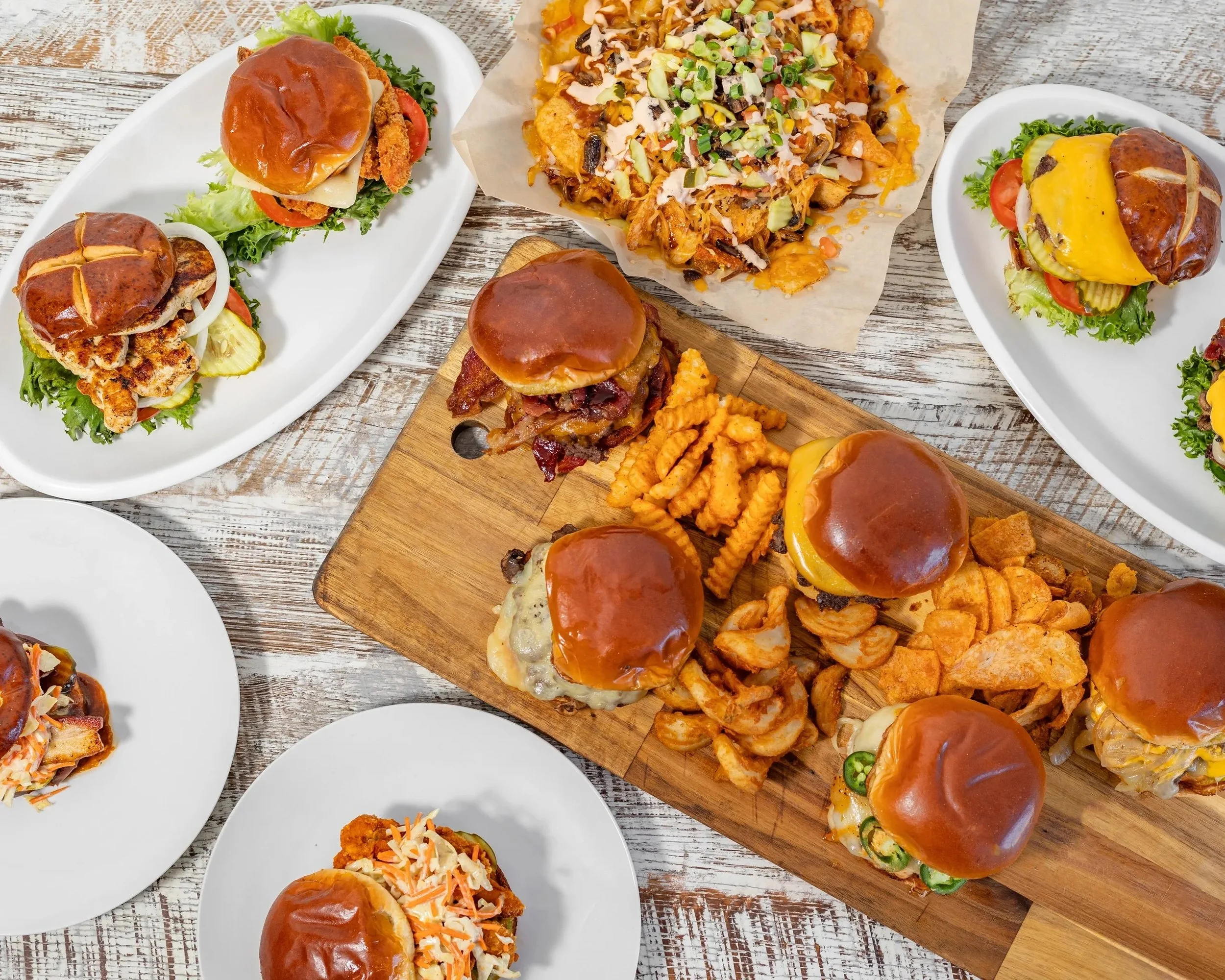Various plates of sandwiches, nachos, and pasta on a rustic wooden table.