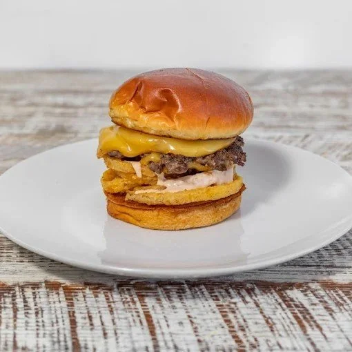 Cheeseburger with melted cheese, burger patty, fried onion rings, and bun, on a white plate.