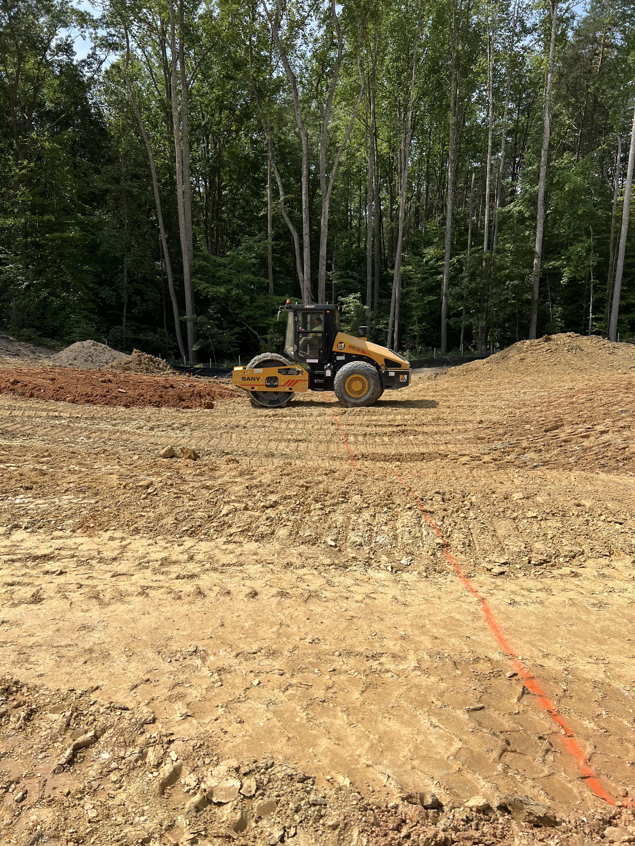Soil compactor performing site preparation and grading on a large construction area marked for earthwork operations.