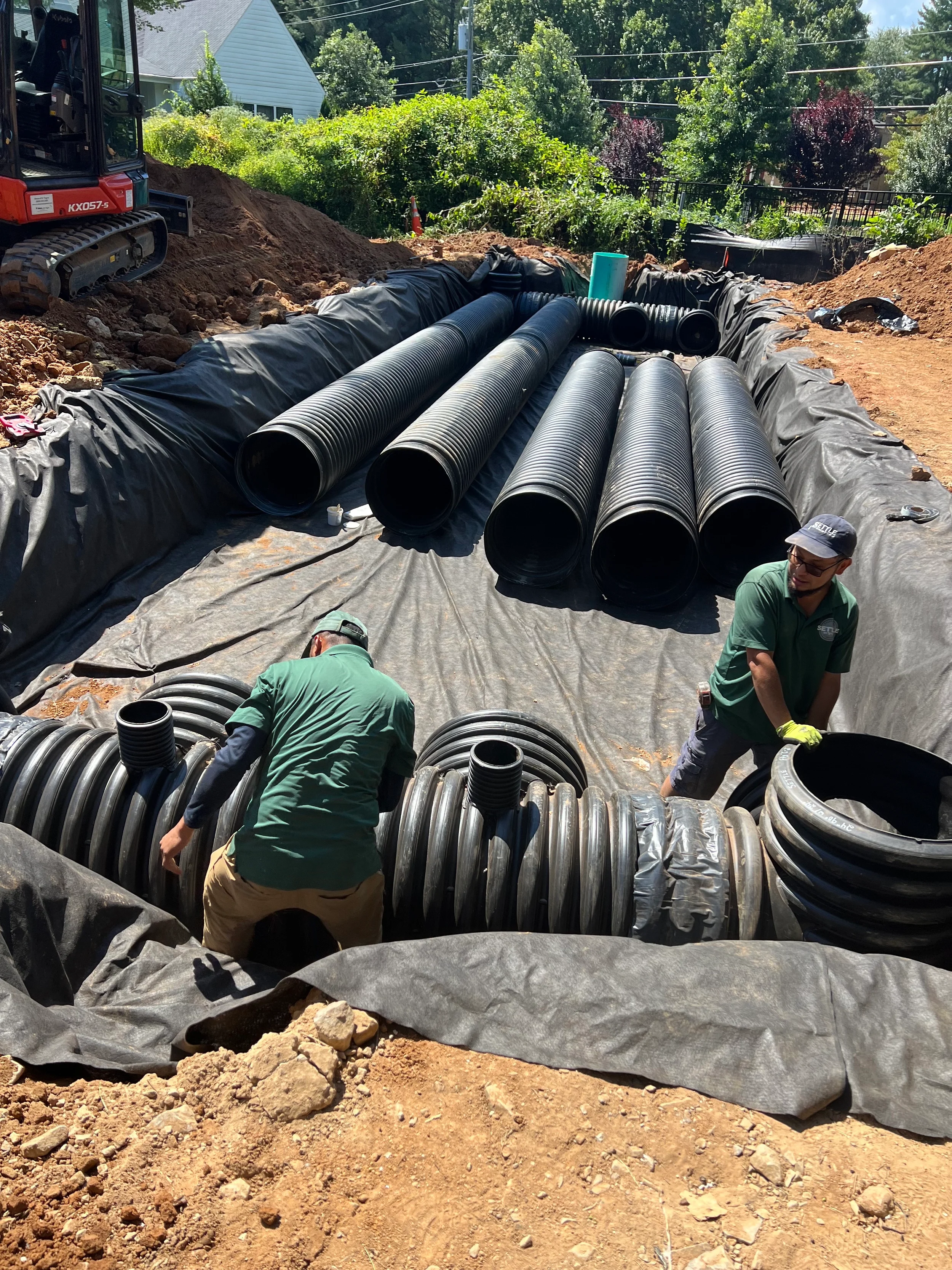 Crew installing corrugated underground pipe detention system over geotextile fabric for stormwater management on a residential site.