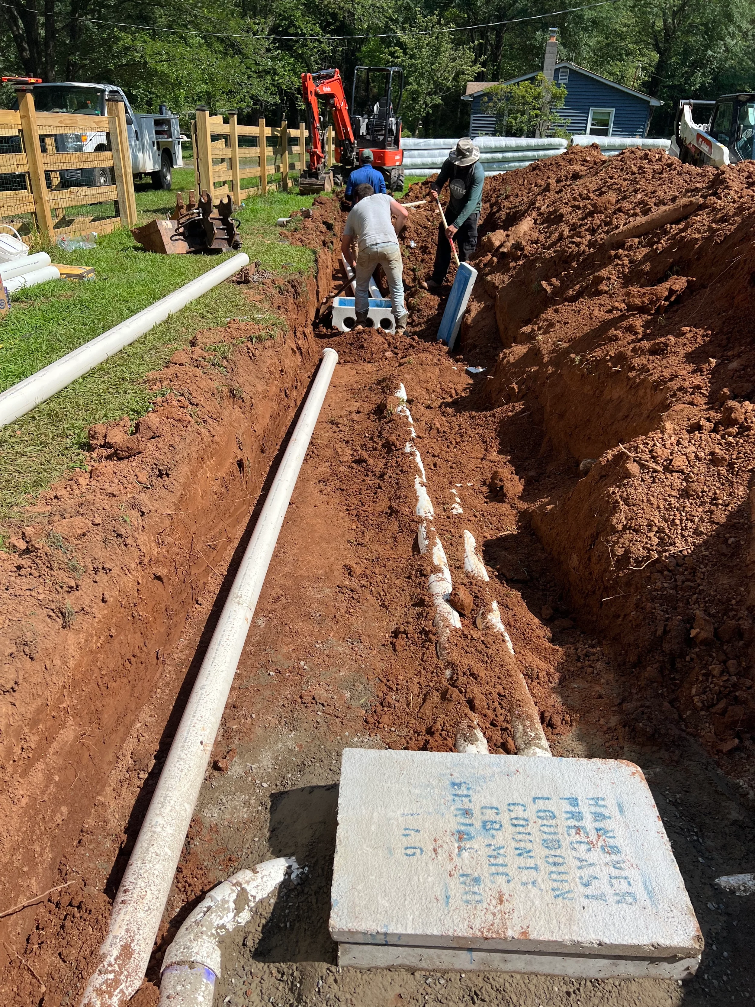 Crew installing PVC septic and drainfield piping in an open trench for a residential onsite wastewater system in Northern Virginia.