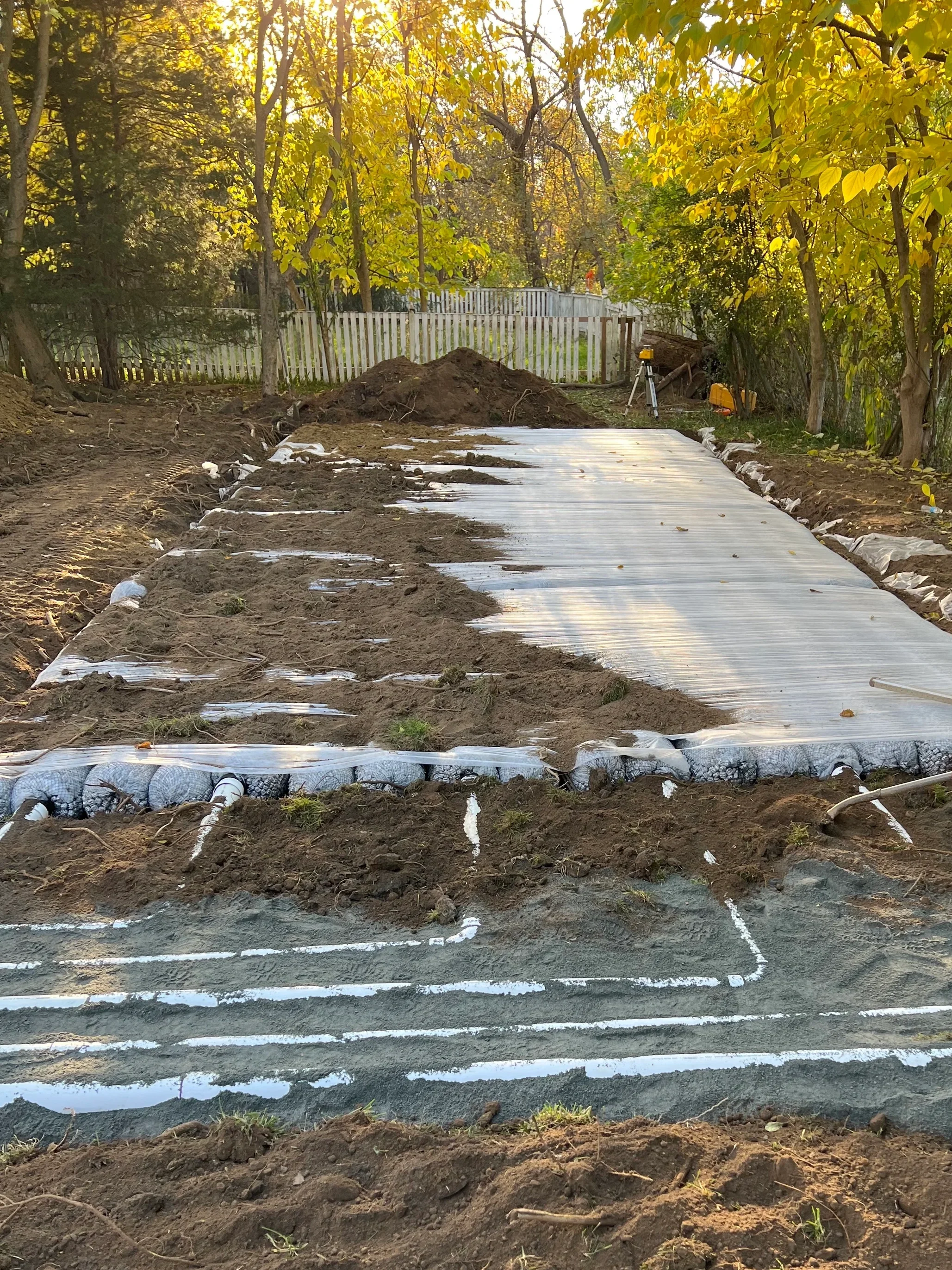Drainfield laterals graded into a sand bed with the system layout chalked out and a silt sock perimeter for erosion control during a septic system installation.