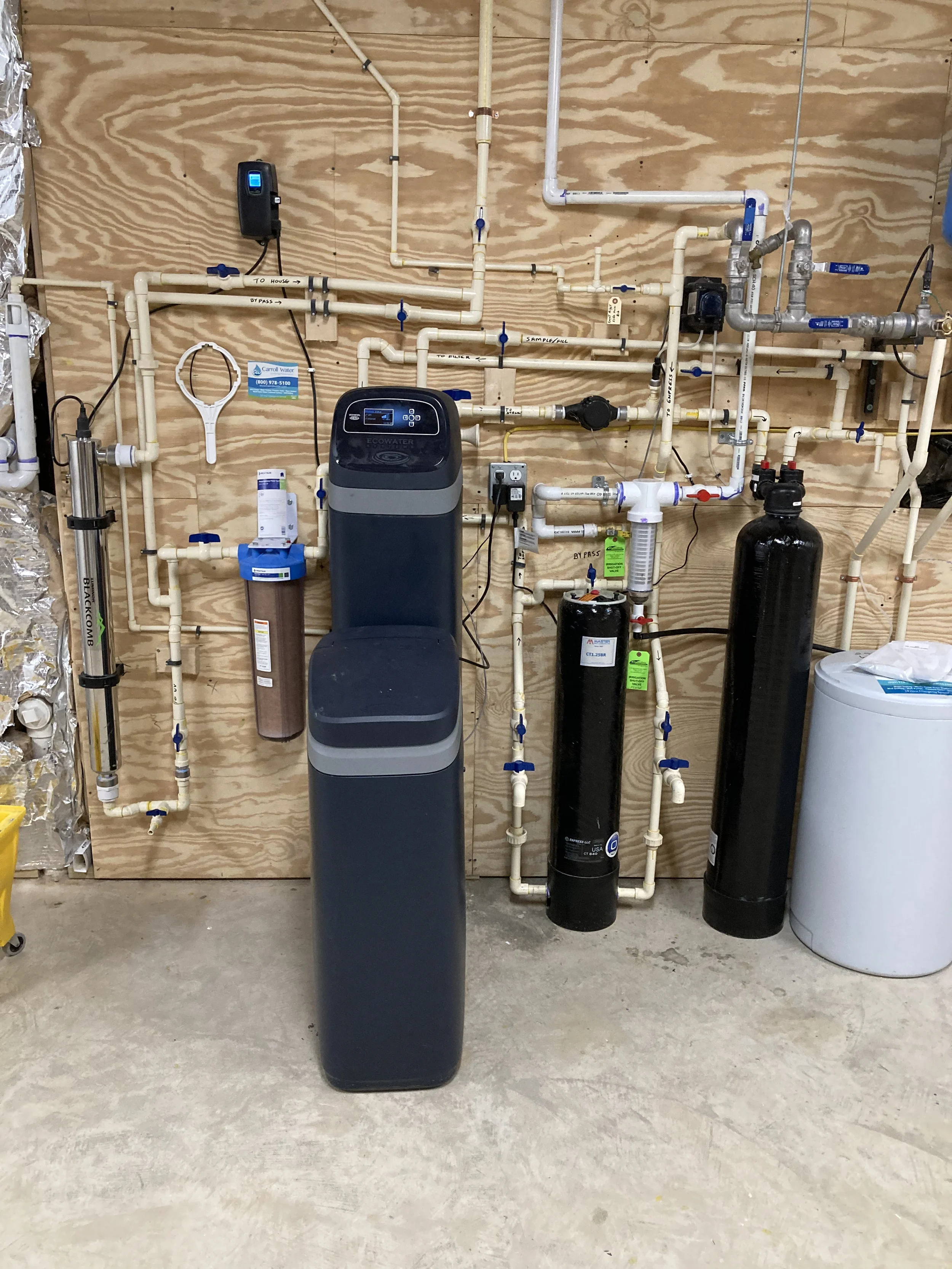 Complete residential well water treatment system installation room with softener, filters, pressure components, and organized plumbing connections.