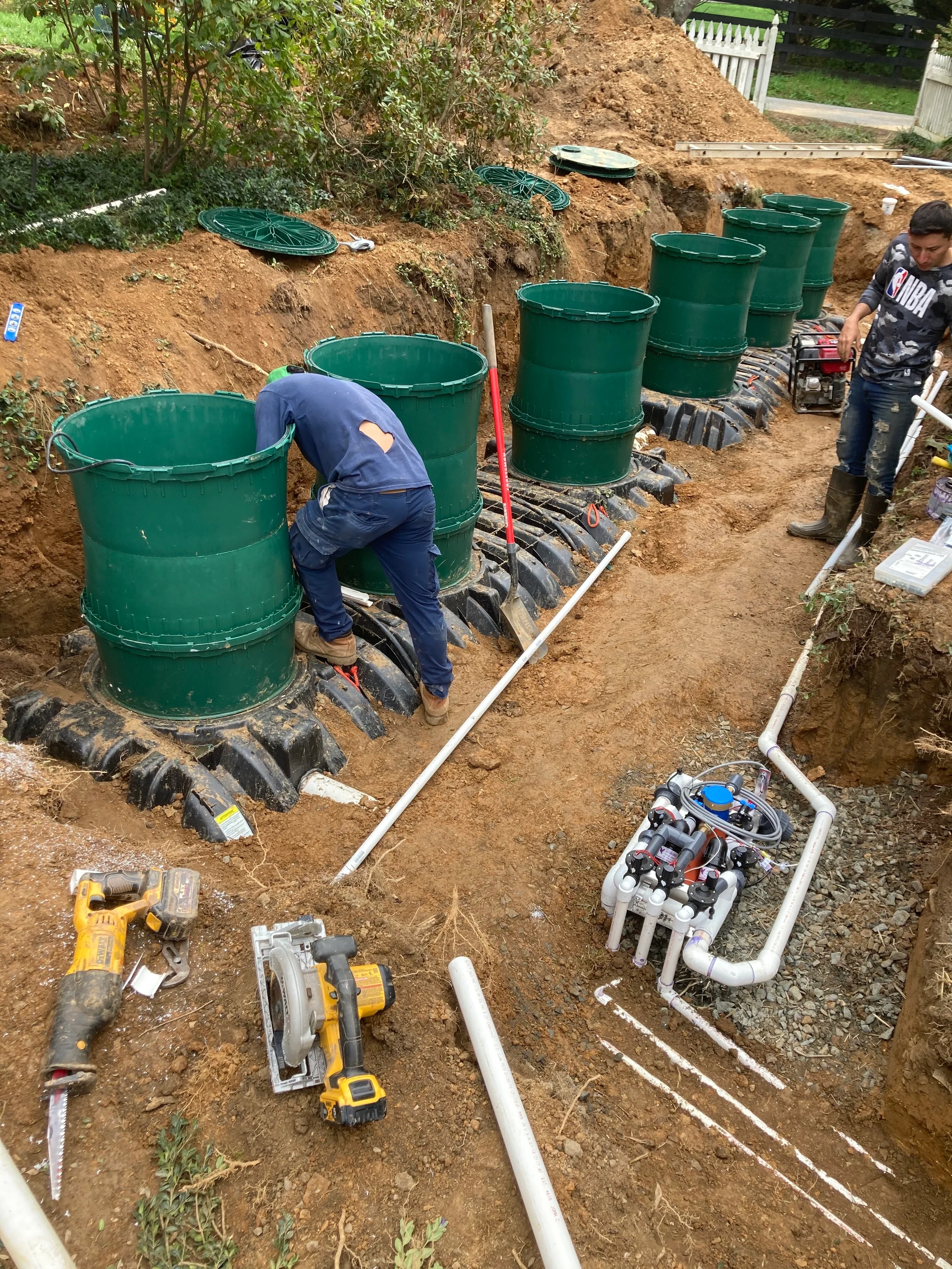Puraflo septic system installation with multiple green risers, treatment modules, PVC piping, tools, and workers inside an excavation.