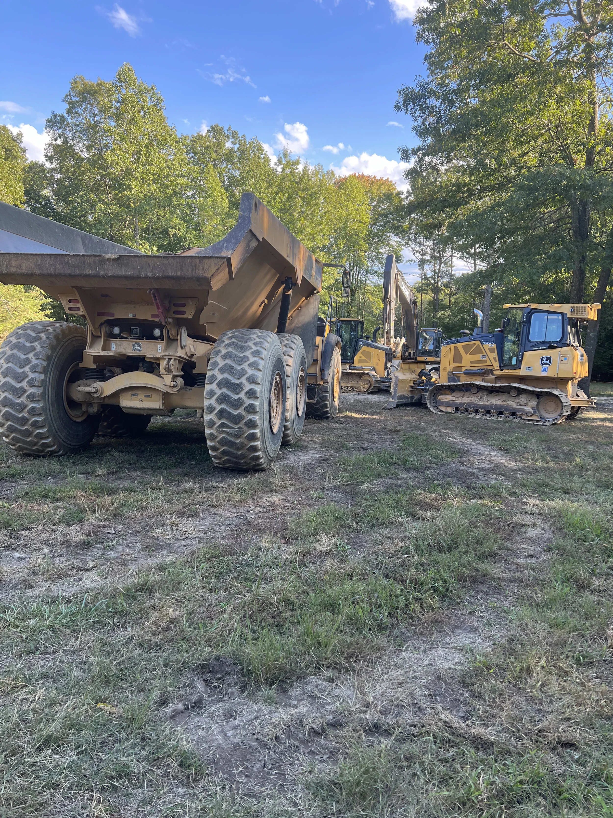 Heavy equipment staged for large-scale earthmoving work including an articulated dump truck, excavator, and crawler dozer.