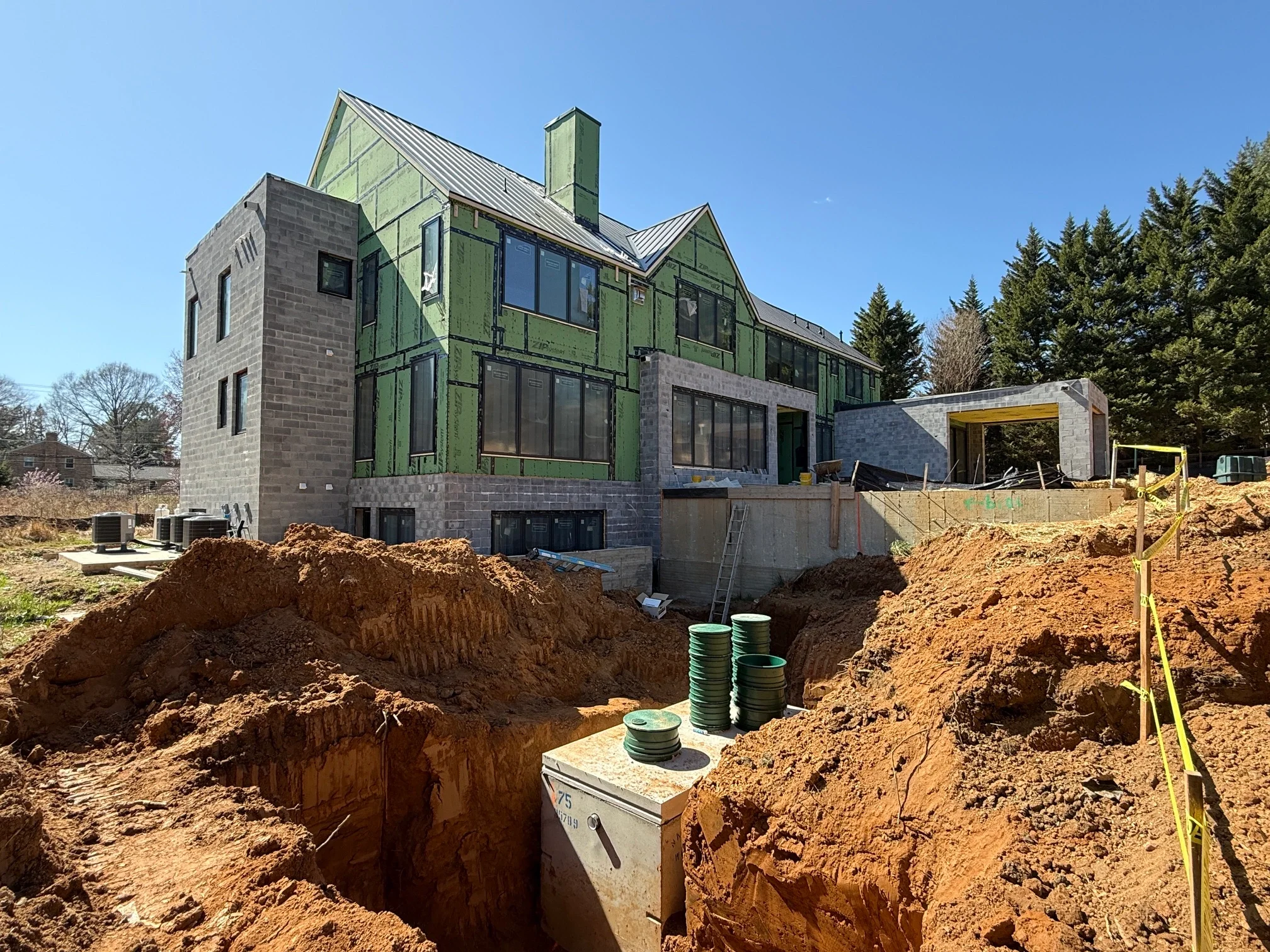 Septic tank in an open excavation in the foreground with a large custom home under construction behind it, an onsite sewage system install in Northern Virginia.