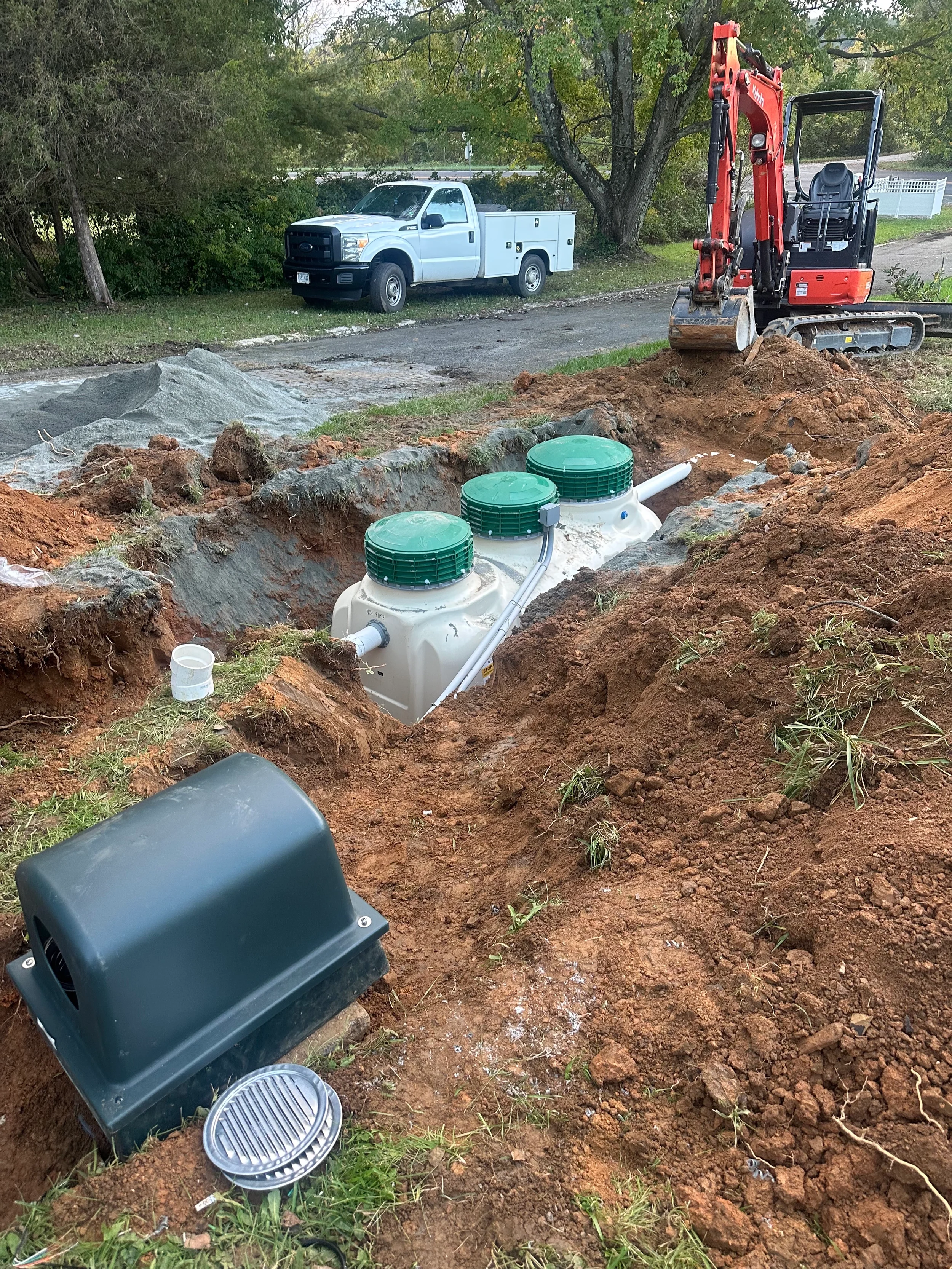 Poly septic tank installation in an excavated residential yard with mini excavator, utility truck, and system components in place.