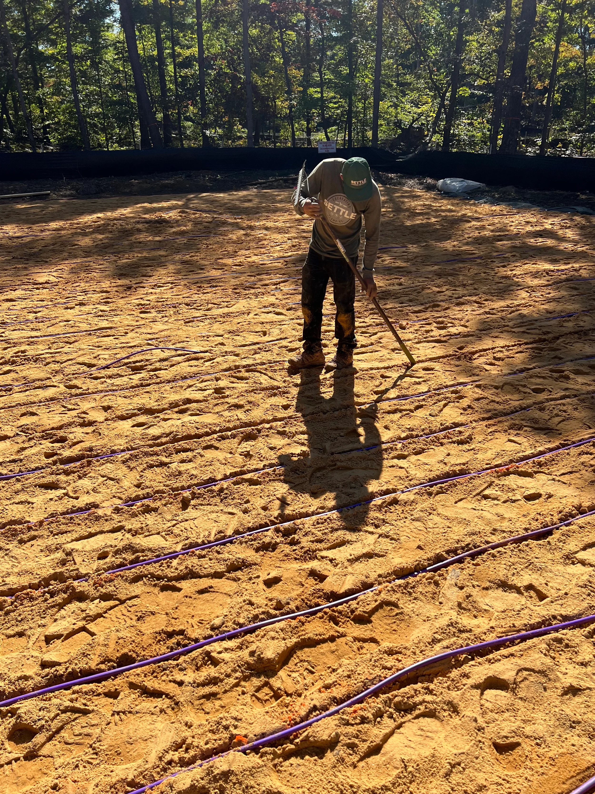 Settle Excavating & Plumbing crew member raking the sand bed of a drip dispersal drainfield, leveling cover over the effluent tubing on a residential septic project.