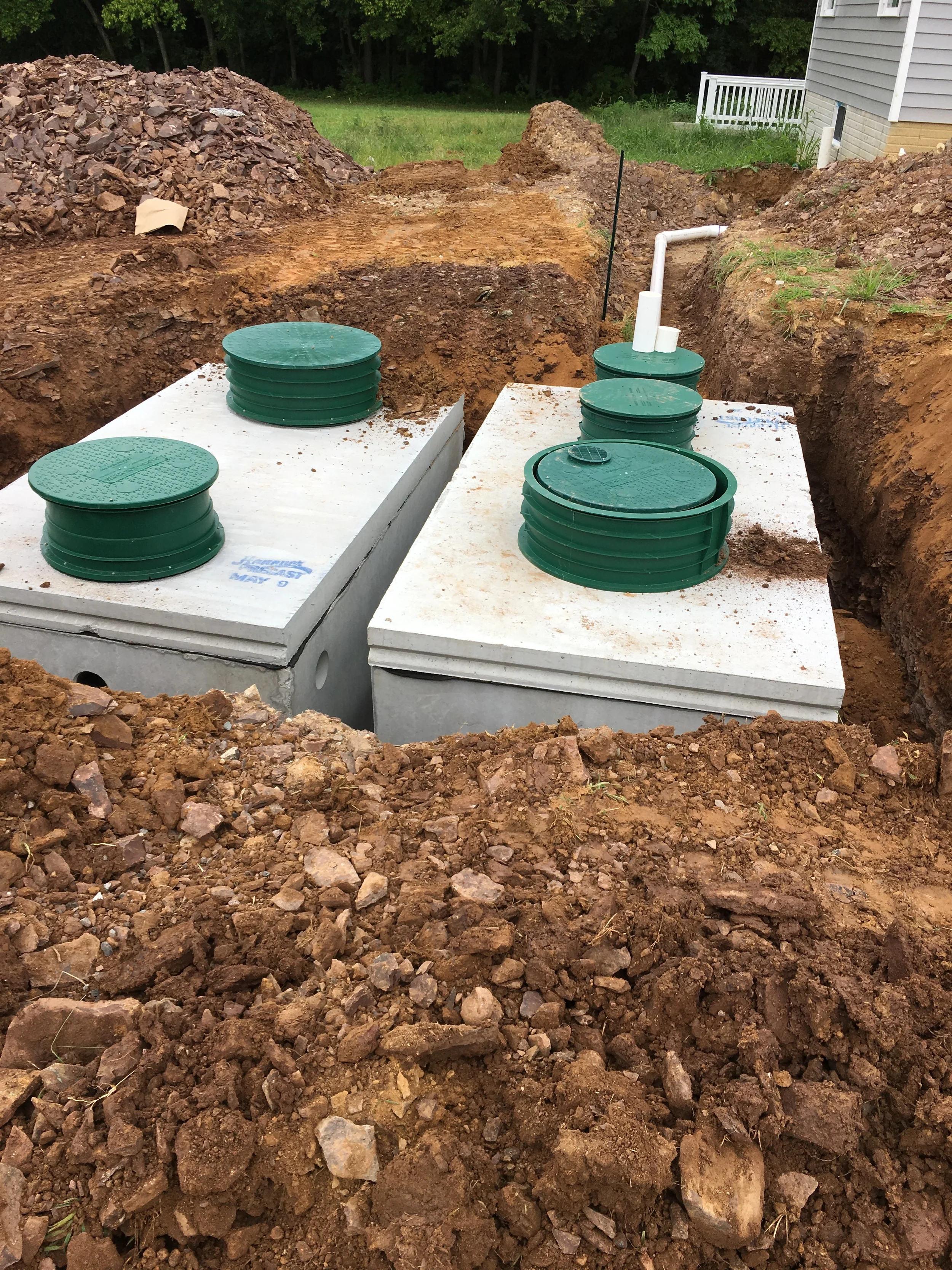 Two precast concrete septic tanks set in an excavated trench with green riser lids during a residential septic system installation in Northern Virginia.