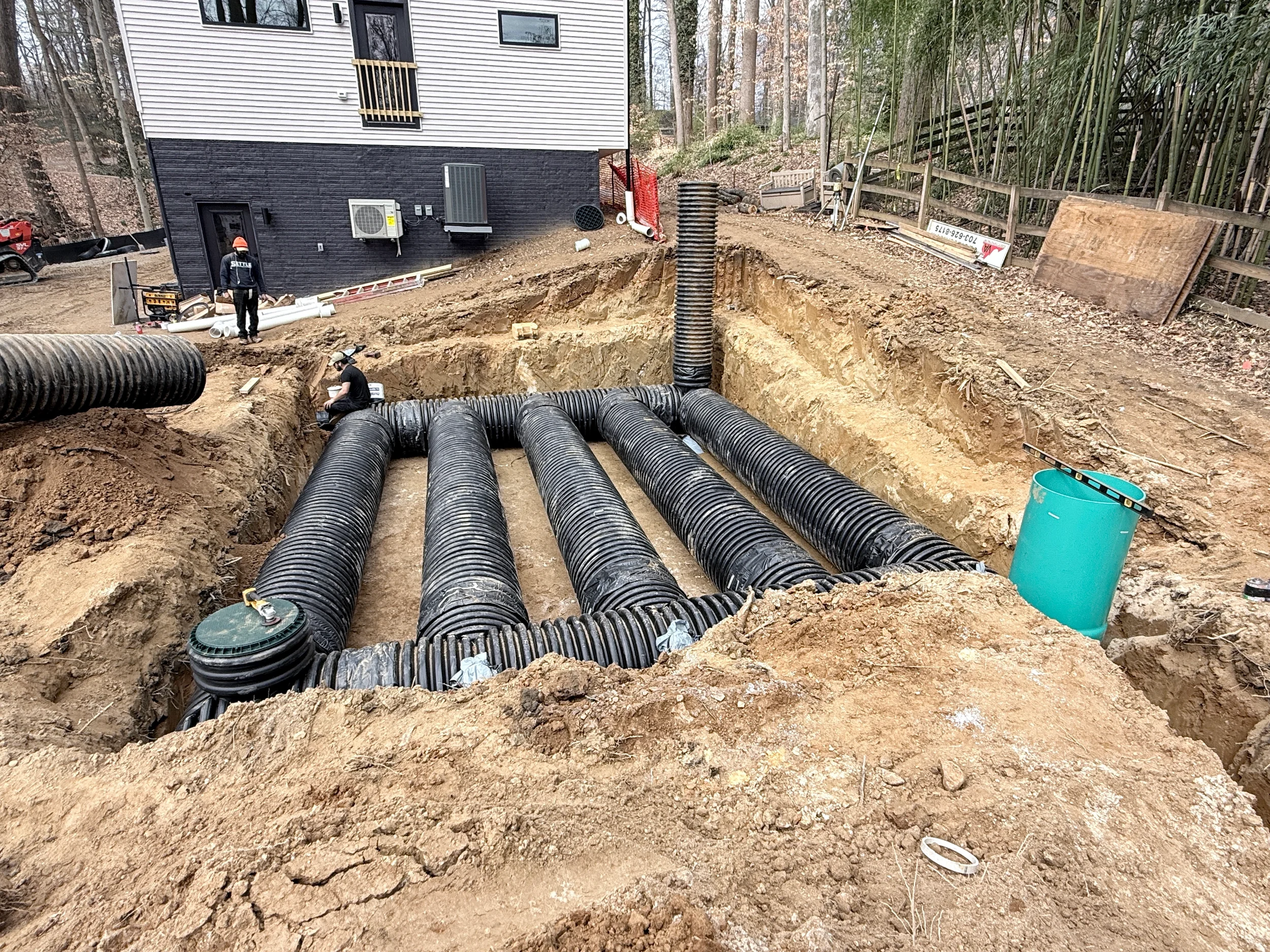 Underground stormwater detention pipe bed with parallel corrugated HDPE pipes, fabric liner, risers, and excavation ready for backfill.
