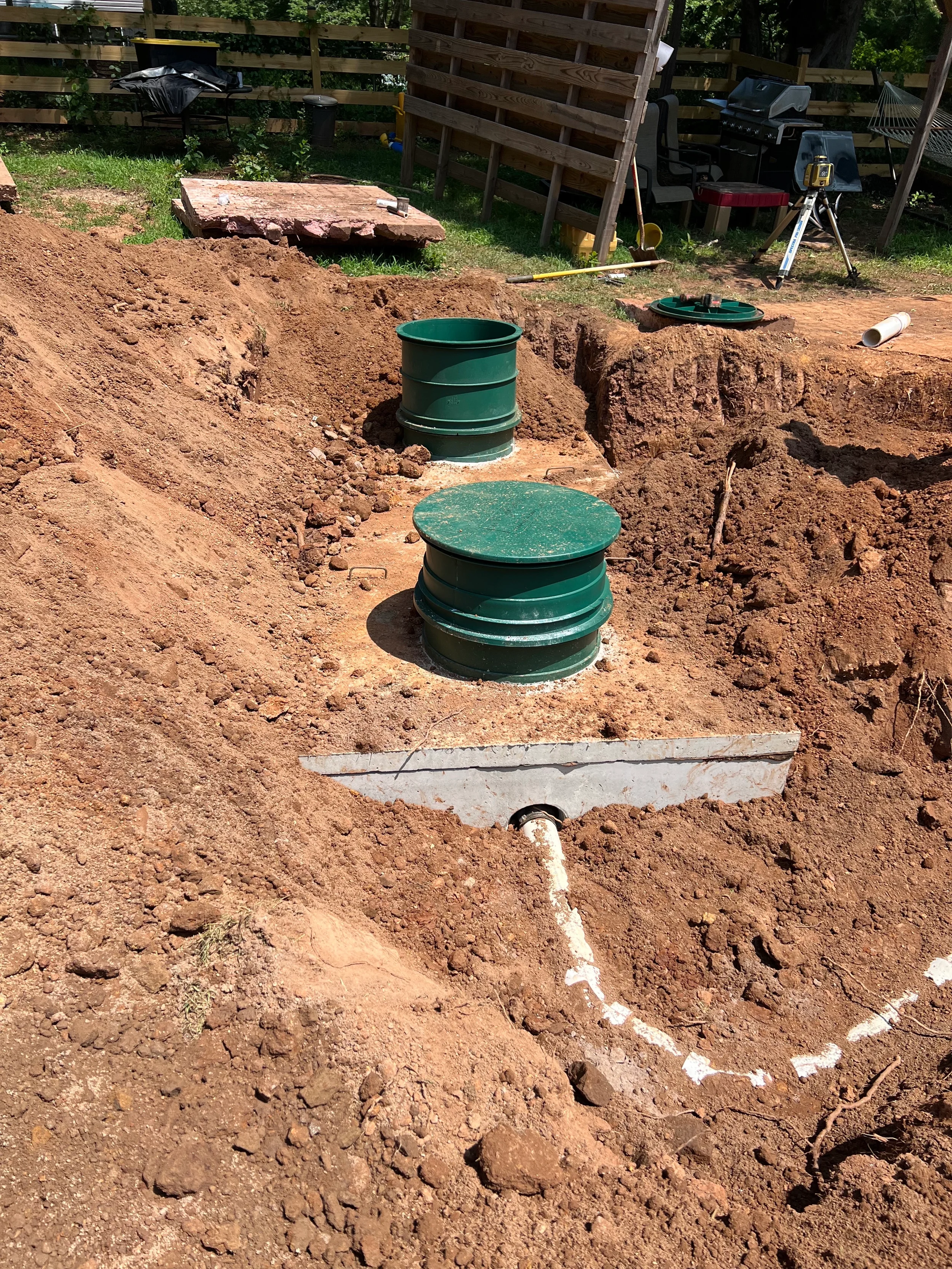 Concrete septic tanks with green access risers installed in a wooded residential yard during onsite wastewater system construction.